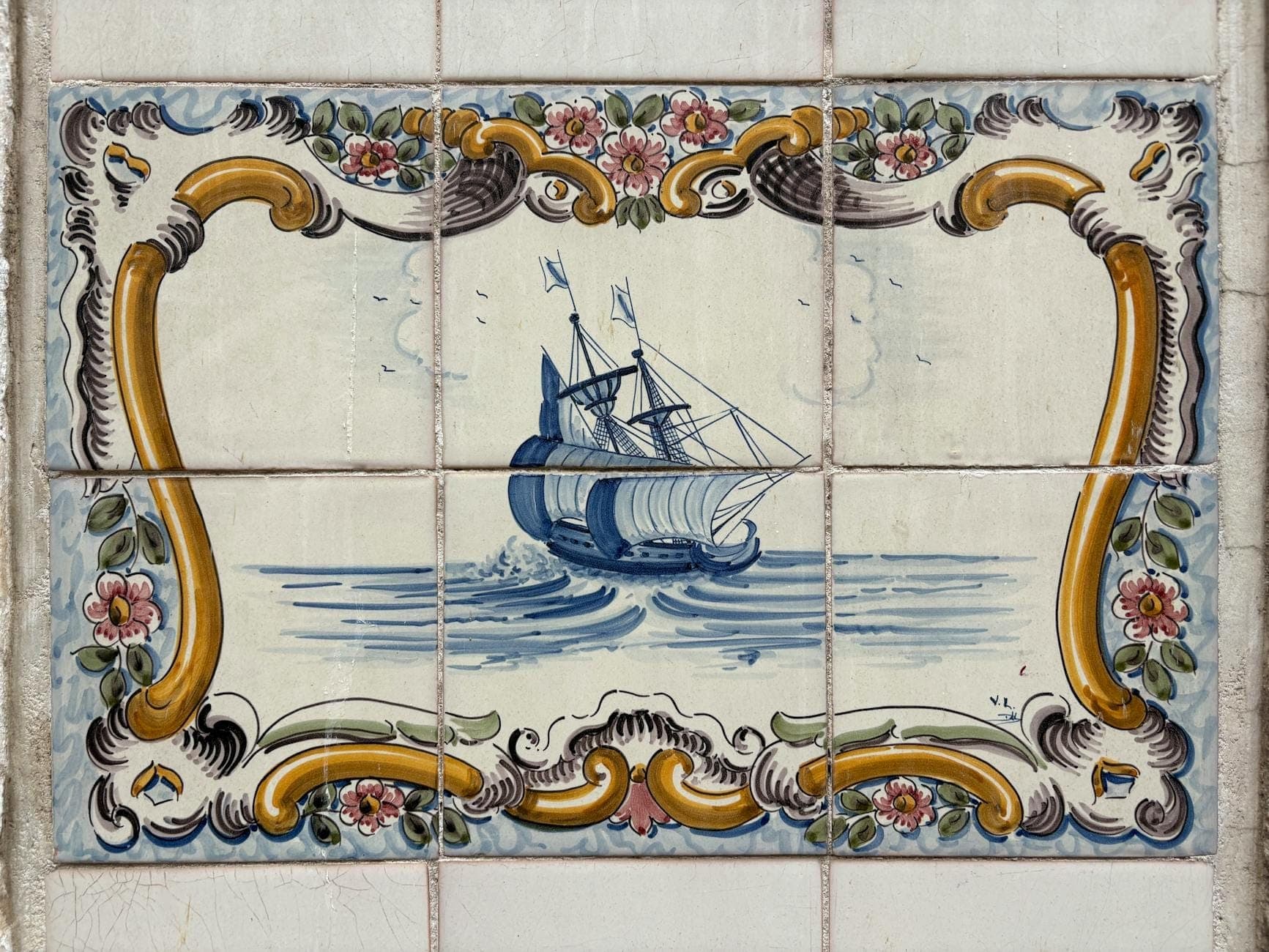 Close-up de um painel de azulejos portugueses tradicionais com um navio pintado, rodeado por motivos florais decorativos.