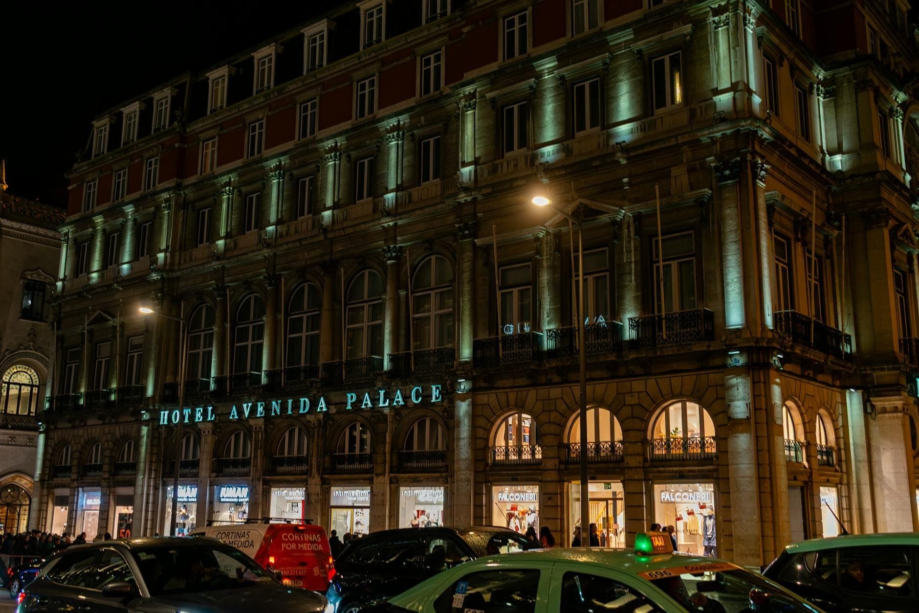 Hotel Avenida Palace em Lisboa iluminado à noite com carros e pessoas em frente à entrada.
