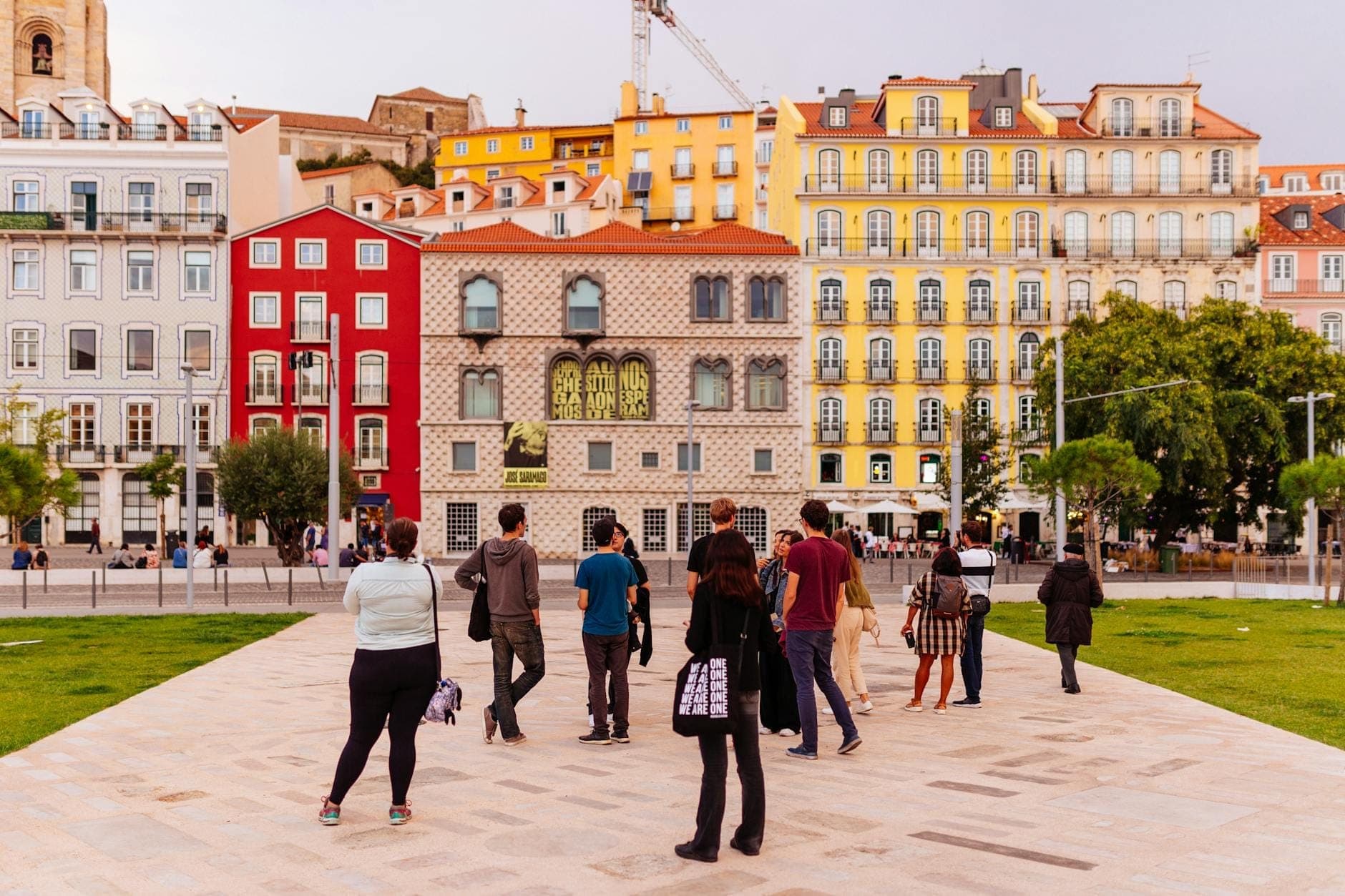 Um grupo de pessoas caminhando juntas por uma praça de pedestres em Lisboa, cercadas por coloridos edifícios tradicionais e a vibrante atmosfera da cidade.
