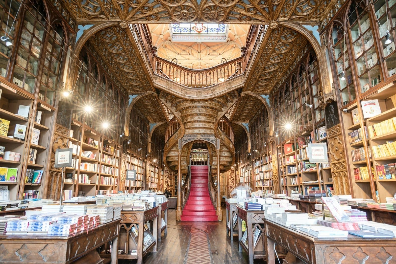 Innenansicht der Livraria Lello mit hohen Bücherregalen, kunstvoll verzierter Holzdecke und der berühmten roten Treppe im natürlichen Licht. Eine einladende und imposante Atmosphäre.