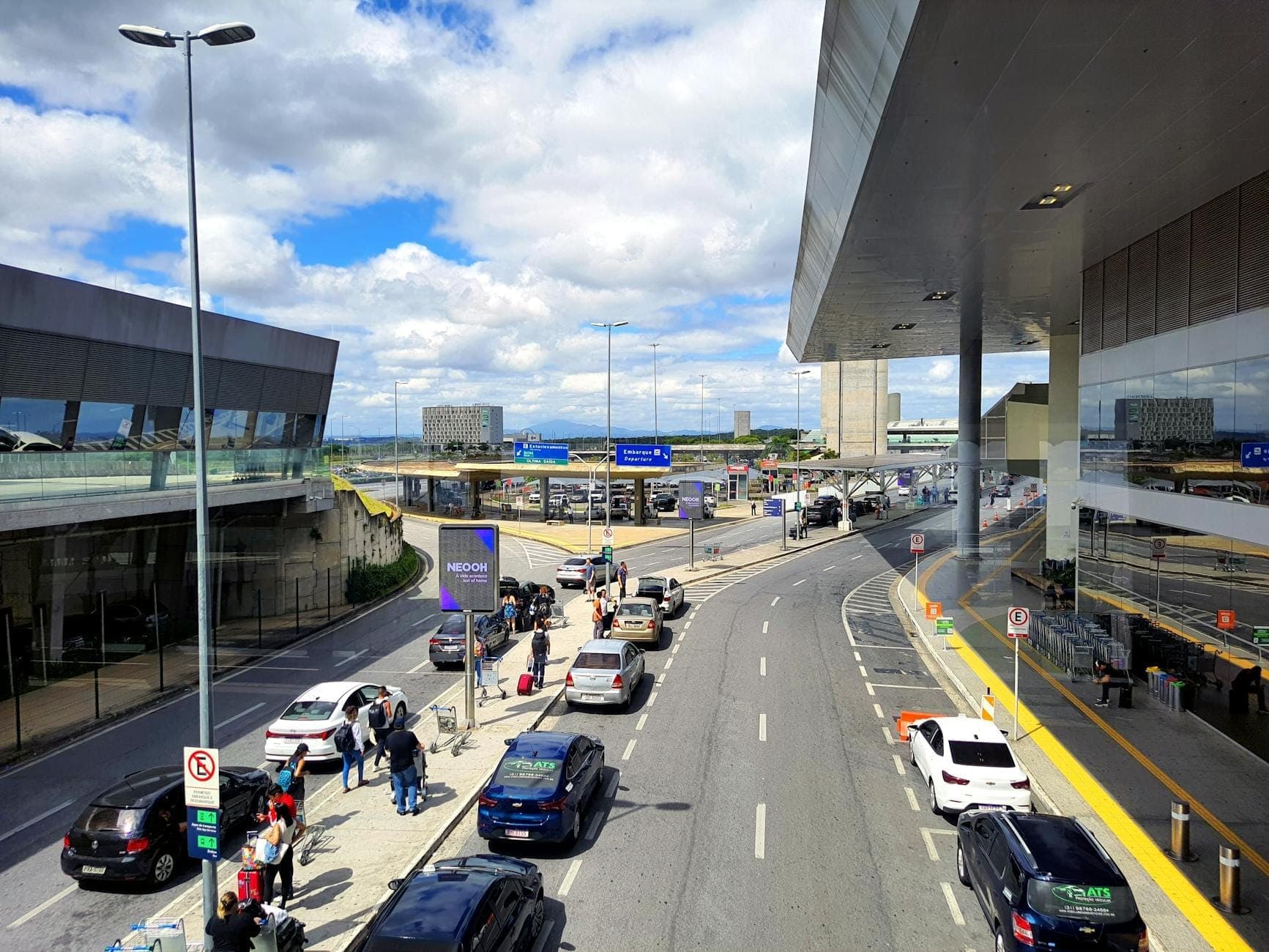 Entrada moderna do aeroporto com carros, táxis e viajantes do lado de fora do Aeroporto de Lisboa Humberto Delgado sob céu parcialmente nublado