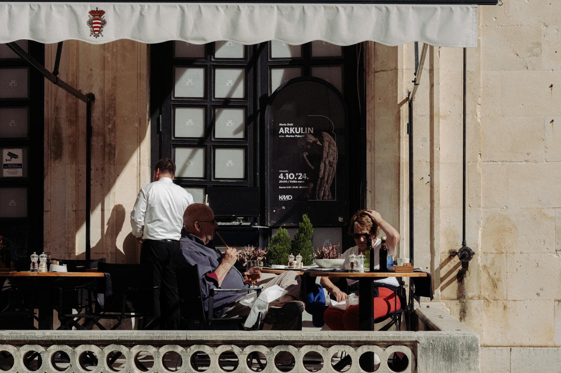 Outdoor-Dining-Szene in einem eleganten Restaurant mit einem Kellner, der sich um die Gäste kümmert, vor der historischen Steinarchitektur von Dubrovnik.