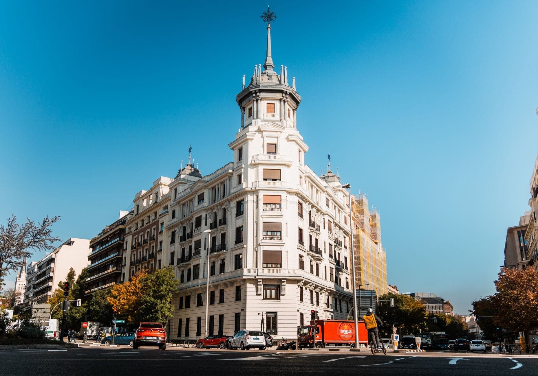 Elegante edificio d'angolo con torre arrotondata e architettura classica, situato in un'ampia strada soleggiata di Madrid con un contesto esclusivo.