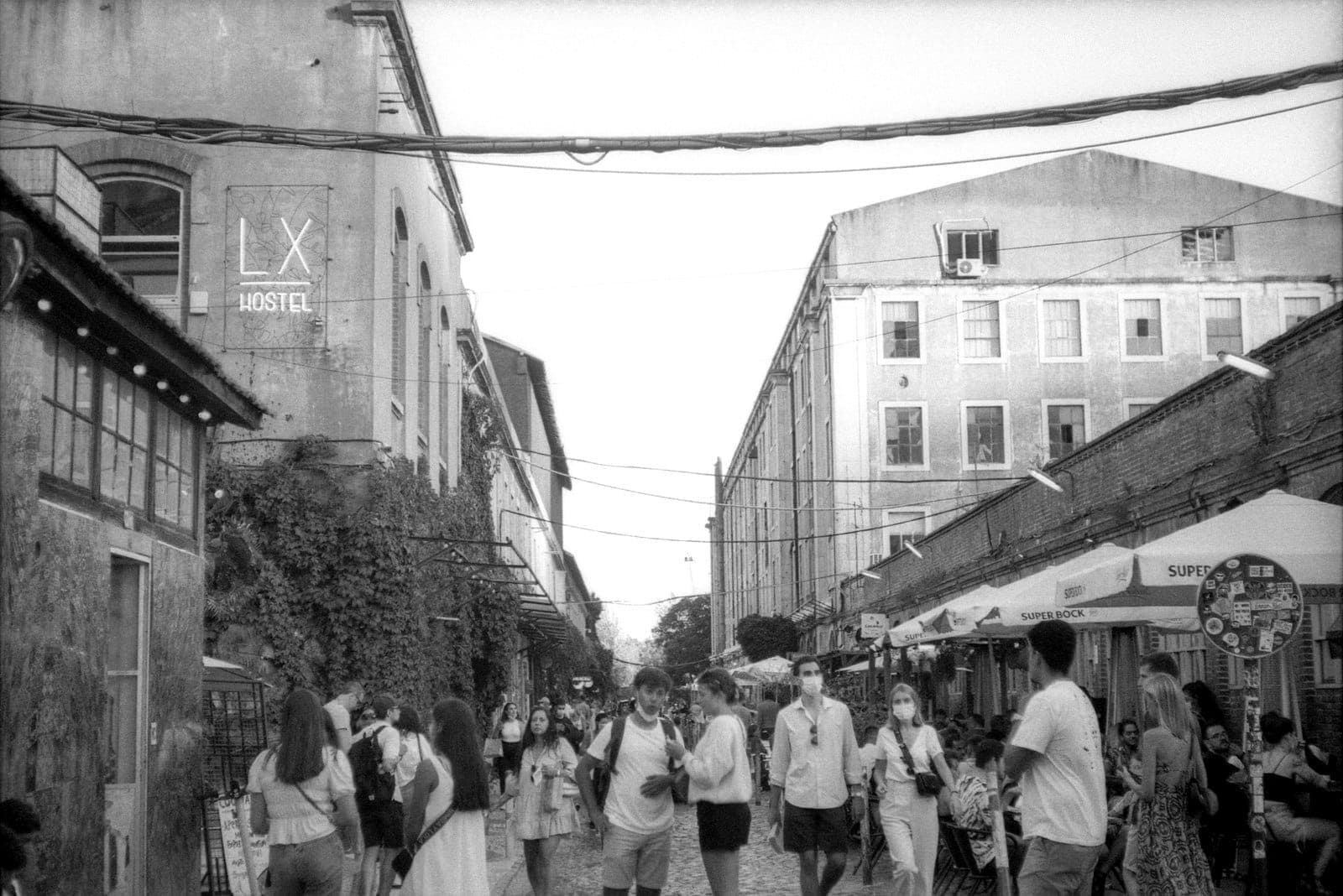 Pátio movimentado da LX Factory com pessoas explorando lojas, prédios industriais históricos, mesas ao ar livre e letreiros criativos no vibrante polo cultural de Lisboa.