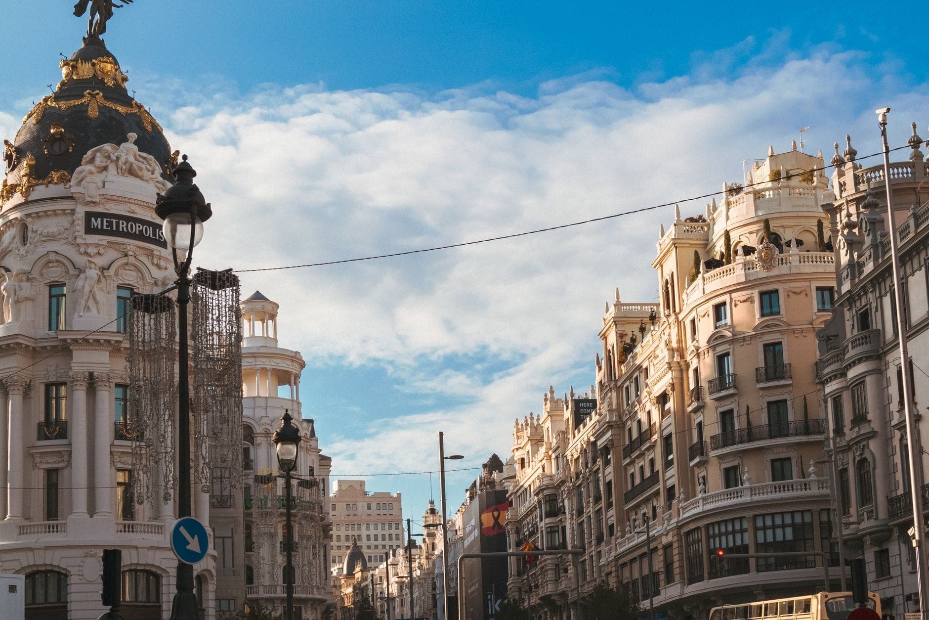 View of Madrid’s Gran Vía with iconic Metropolis building and elegant early 20th-century façades under a blue sky.