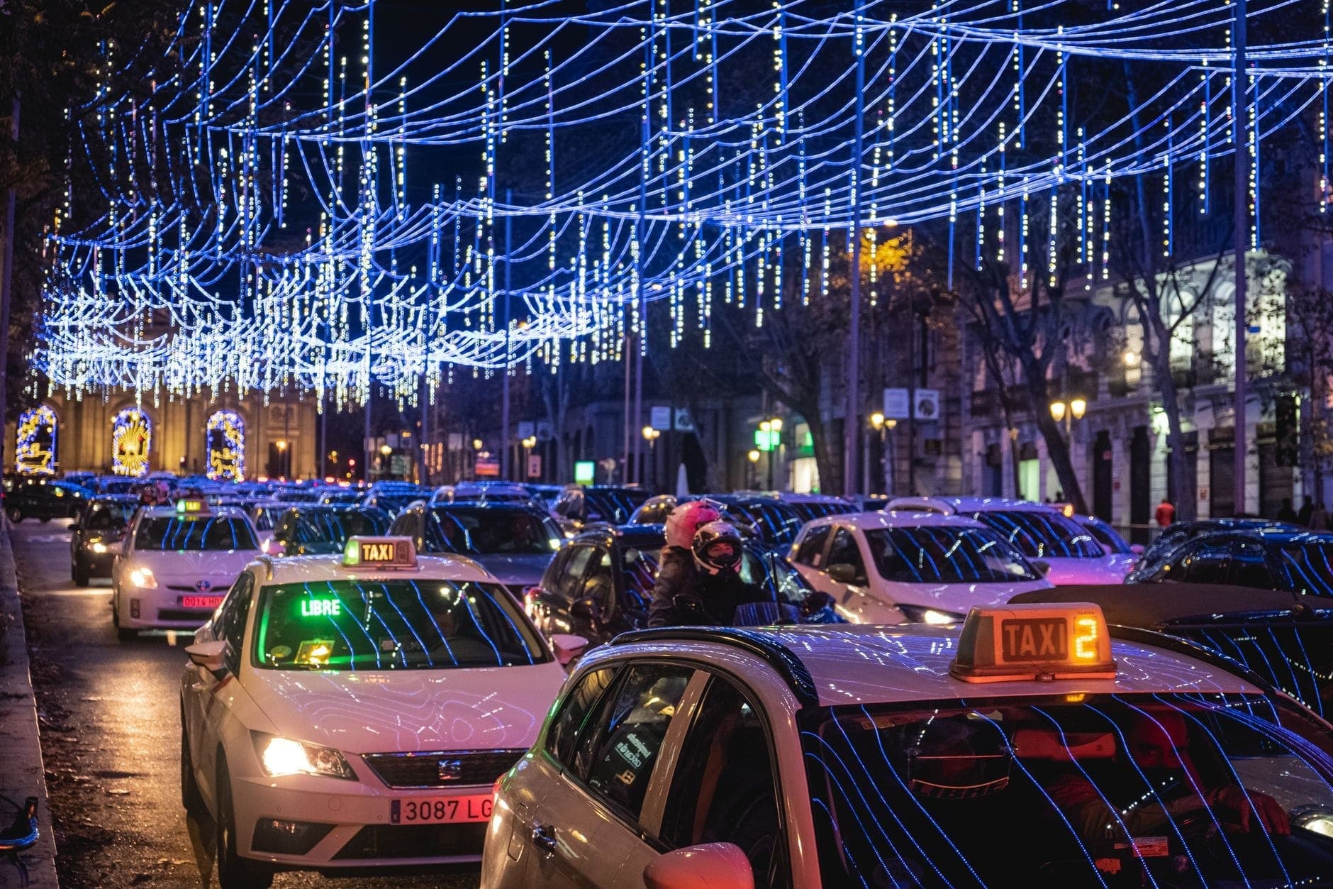 Cảnh phố đêm tại Madrid với đèn Giáng sinh màu xanh lam được giăng trên cao và các xe ô tô, bao gồm cả taxi, trong dòng giao thông phía dưới những ánh đèn lễ hội.