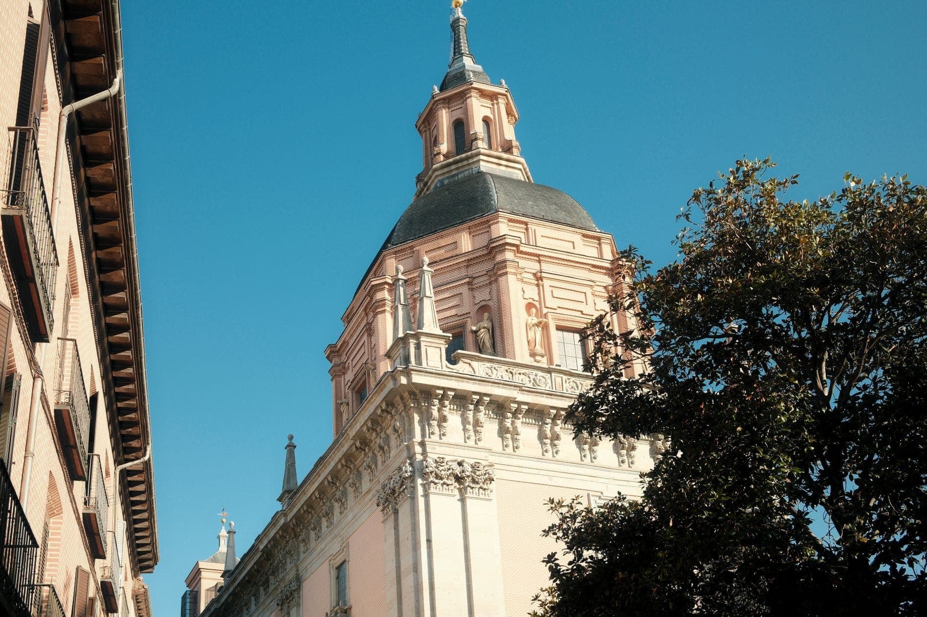 Sunlit exterior of a historic Madrid church with a Baroque dome, viewed from the street with blue sky above.