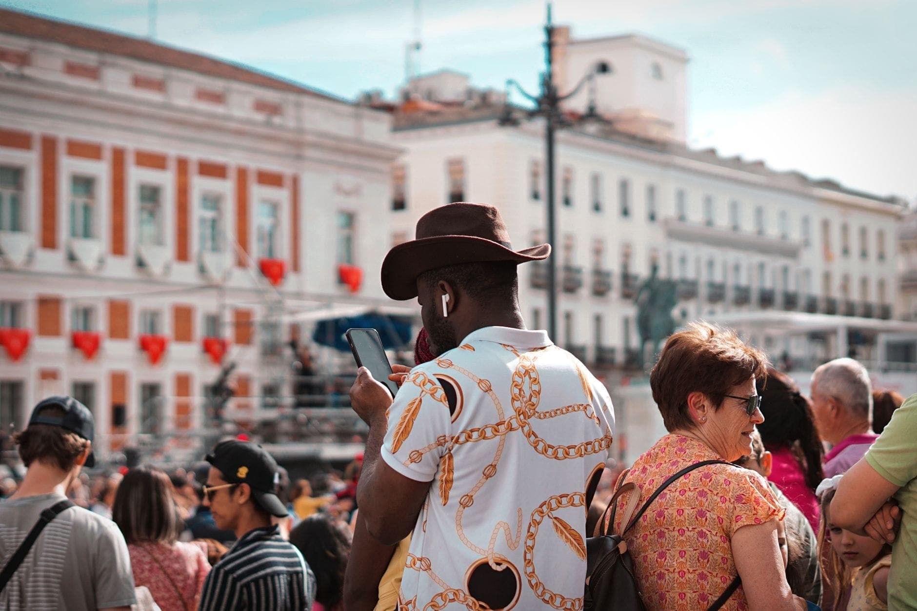 Multidão de pessoas na Puerta del Sol de Madrid, com edifícios característicos ao fundo e turistas se misturando, mostrando uma movimentada cena urbana.