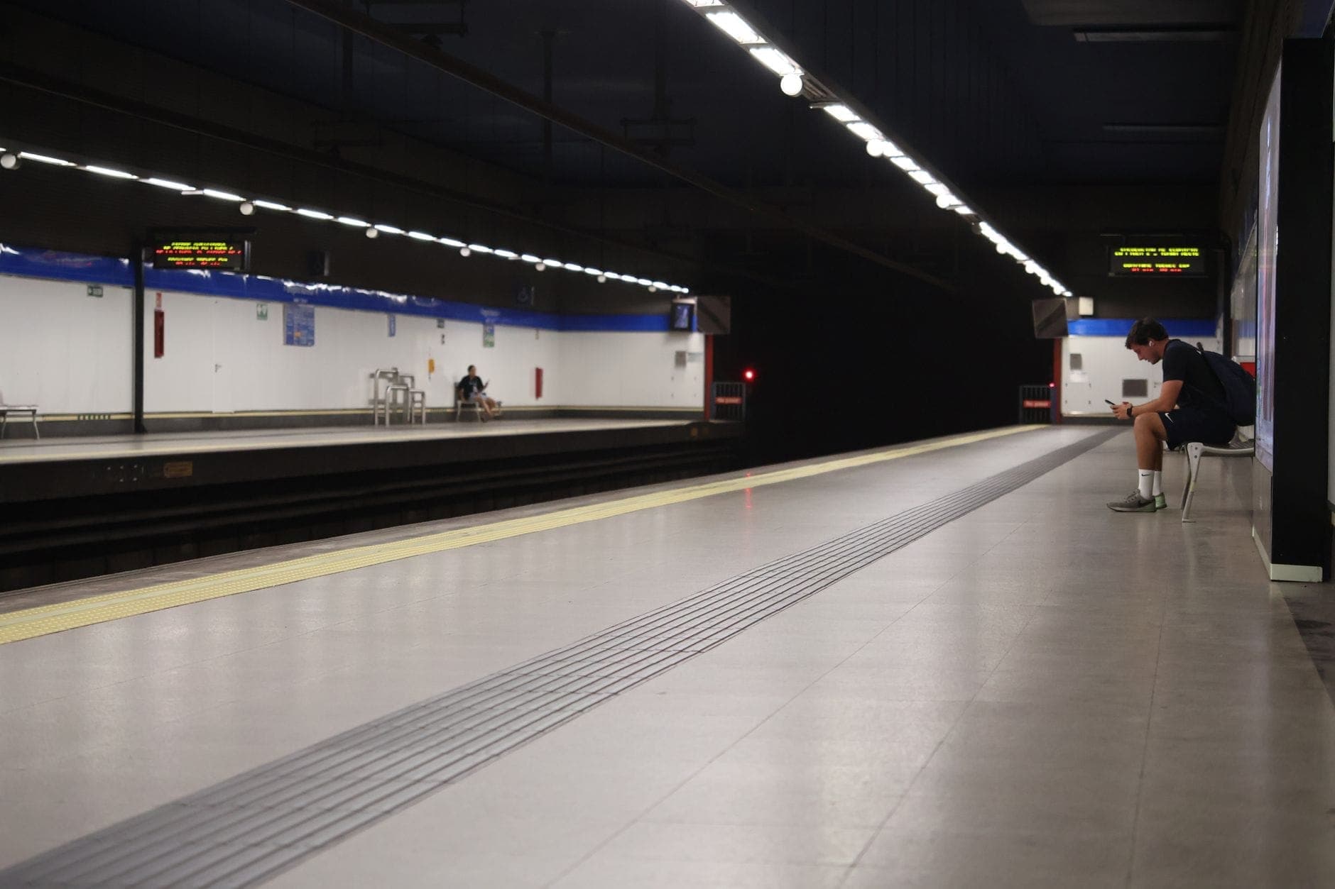 Plataforma moderna de estação do Metro de Madrid com passageiros à espera e sinalização clara, bem iluminada e típica do sistema de metrô da cidade.