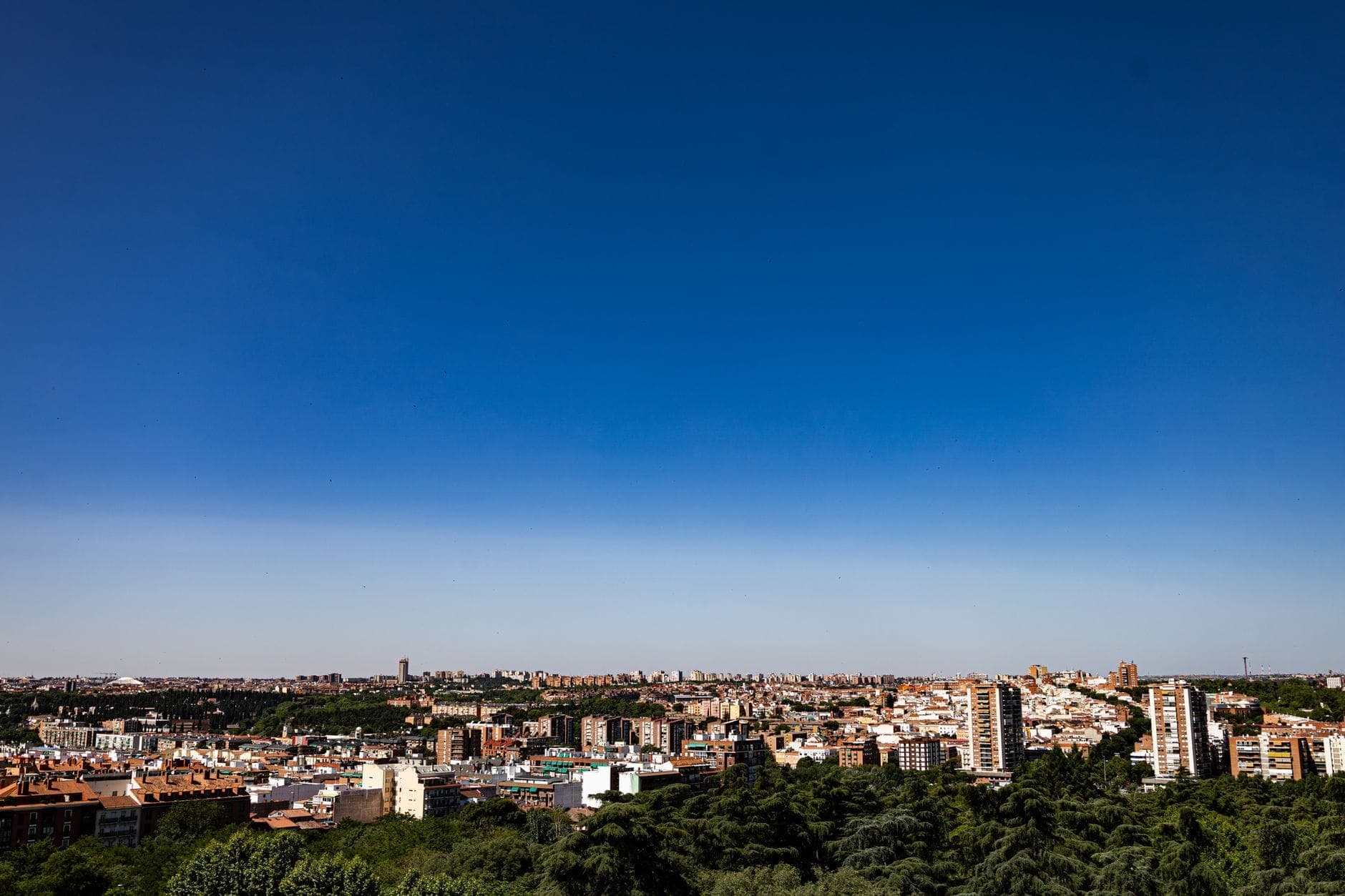 Ampla paisagem urbana de Madrid sob um céu azul profundo e sem nuvens, mostrando edifícios e intensa luz solar de verão.