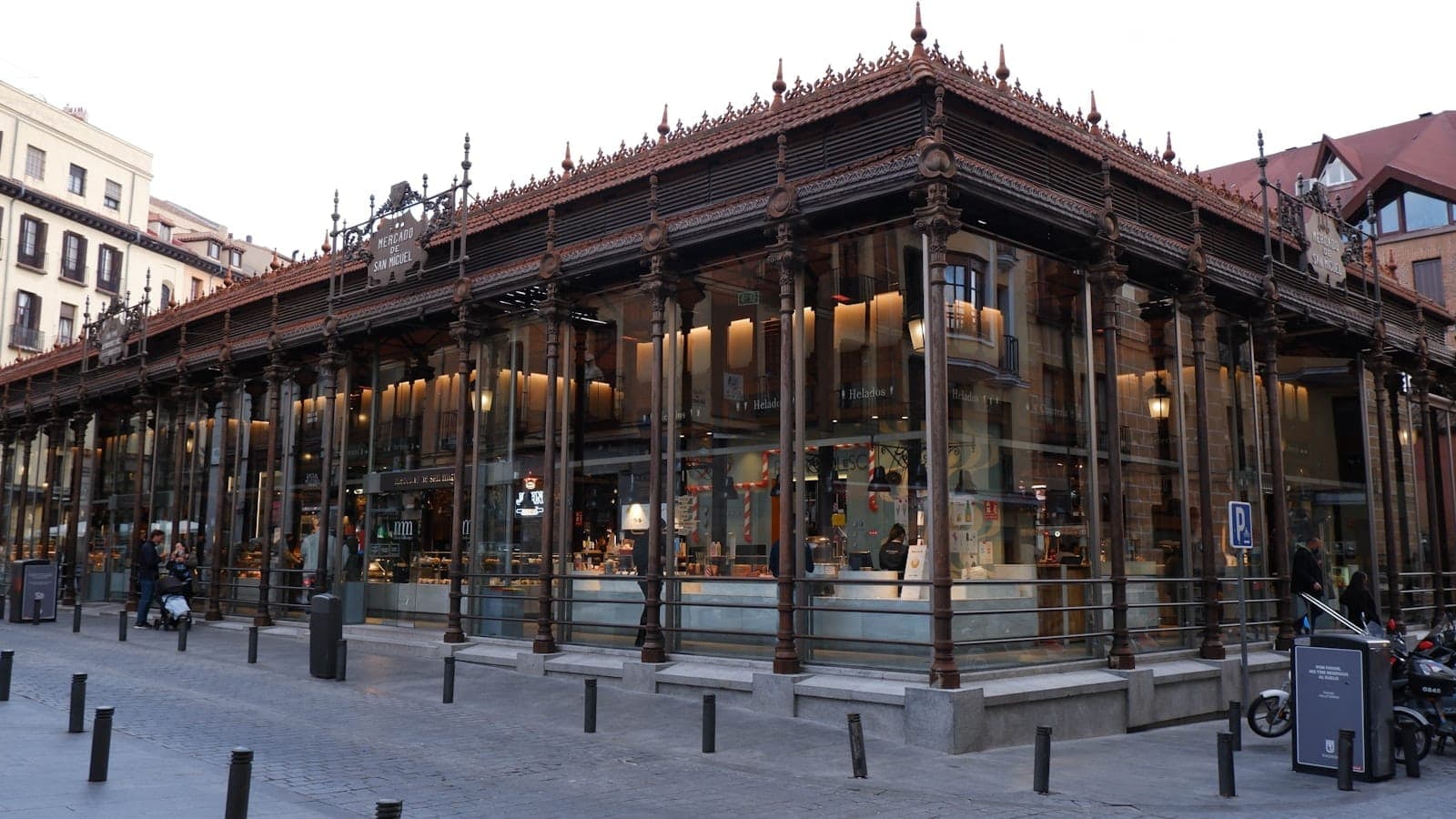 Vista esterna del Mercado de San Miguel di Madrid, un vivace mercato in vetro e ferro noto per le sue bancarelle di cibo e tapas, con persone visibili all'interno.