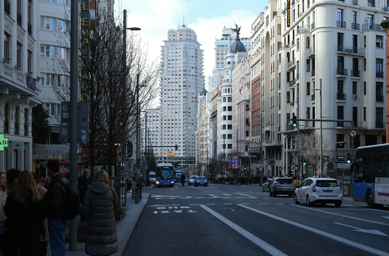 Gran Vía nel centro di Madrid con persone che indossano cappotti invernali e alberi spogli lungo il viale sotto un cielo sereno