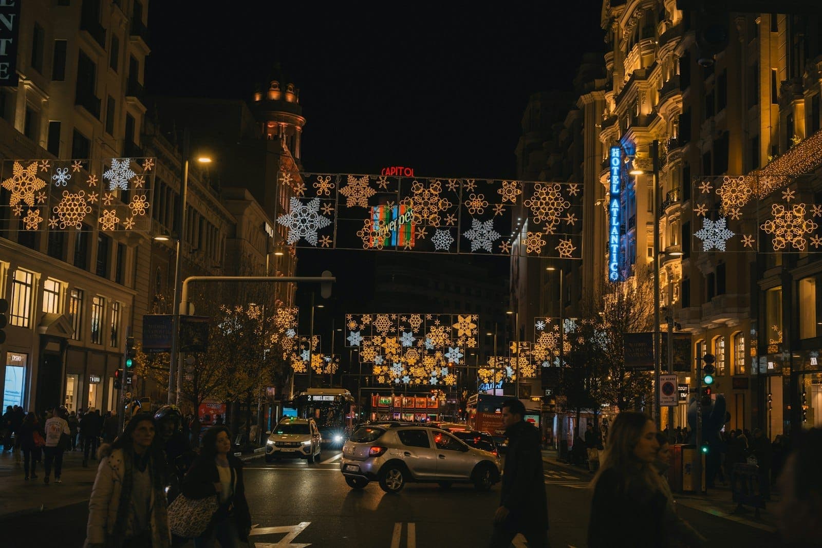 Scena notturna sulla Gran Vía di Madrid con luci natalizie festive appese sopra una strada affollata e gruppi di persone.