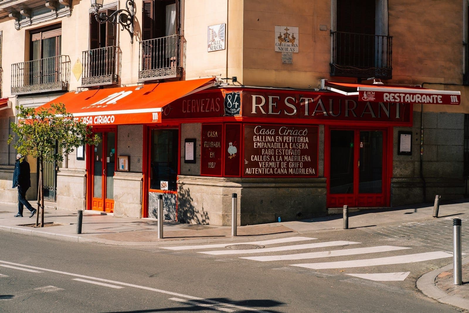 Vista della strada di un ristorante economico a Madrid con tenda rossa e bacheca del menu all'esterno, ideale per assaporare il menú del día.