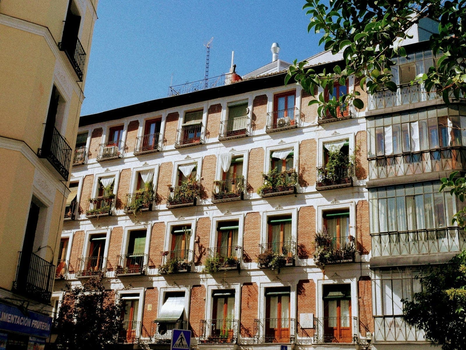 Tradizionale palazzo di appartamenti a Madrid con molti balconi e piante, che mostra opzioni di alloggio locale conveniente in un quartiere centrale.