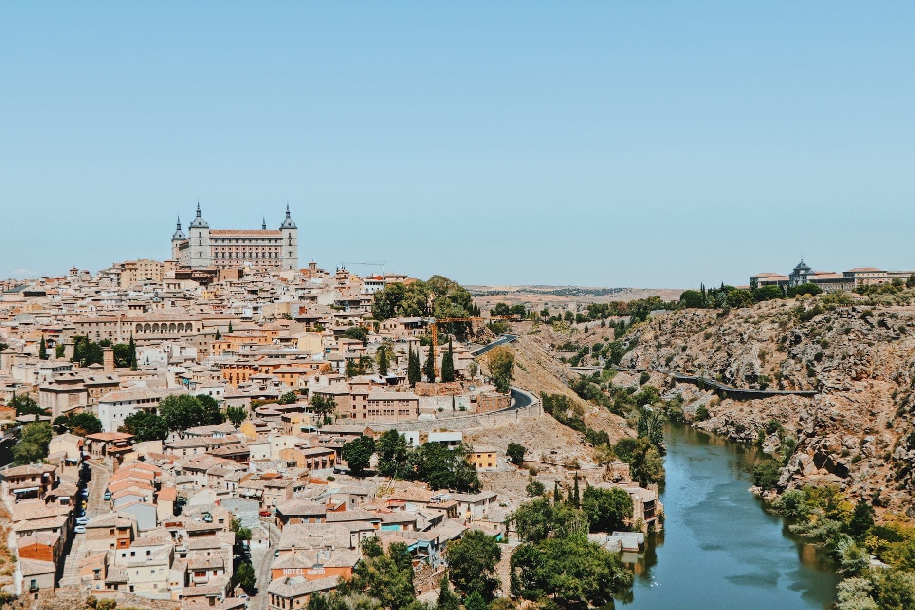 Vista panoramica dell'antica città di Toledo, del fiume e dell'Alcázar sotto un cielo azzurro limpido, che mostra perché è una classica gita di un giorno da Madrid.