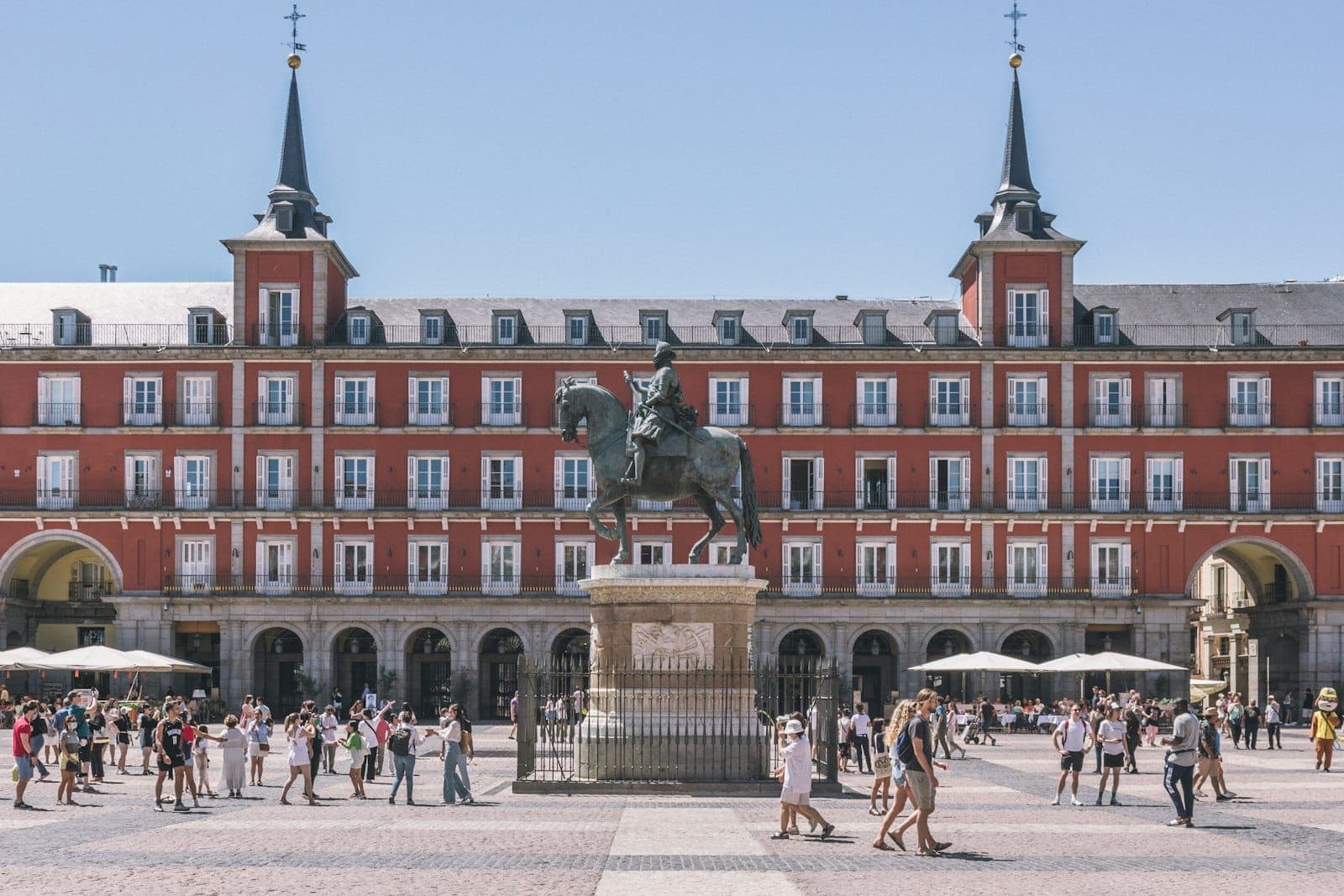 Belebte Szene auf der Plaza Mayor in Madrid mit Touristen und der Reiterstatue im Zentrum, historische Gebäude im Hintergrund.