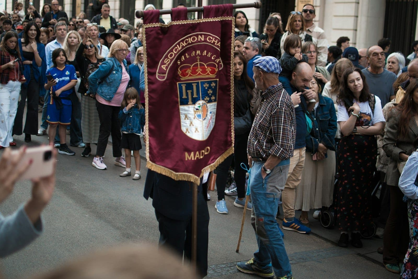 Procesión callejera en Madrid con una pancarta que dice 'Madrid' rodeada de una multitud de espectadores.