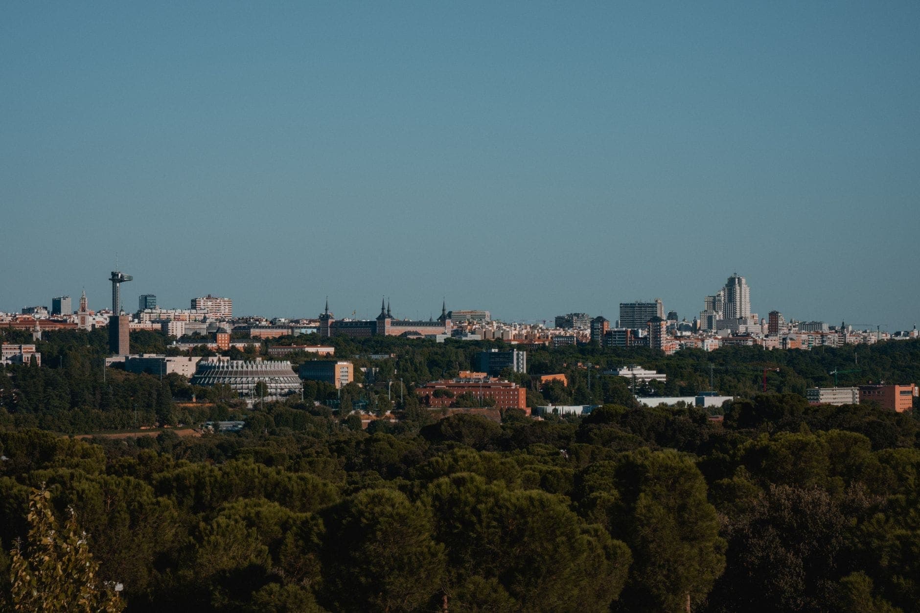 Vista panorámica de Madrid con parque verde y horizonte urbano, mostrando varios barrios y monumentos de la ciudad.