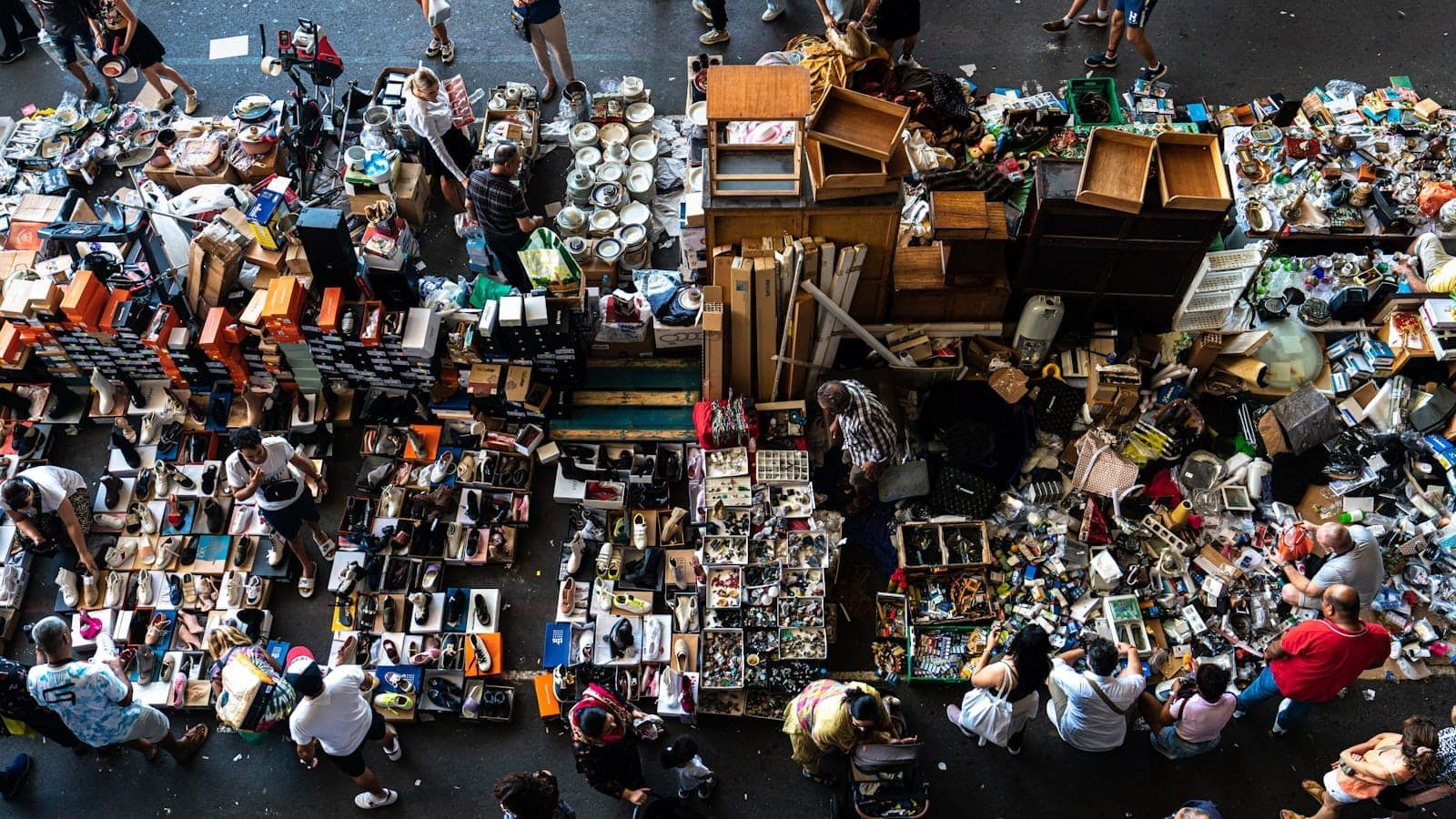 Luftaufnahme eines belebten Flohmarkts mit Ständen, die verschiedene Antiquitäten, Sammlerstücke und Secondhand-Waren verkaufen, umgeben von Einkäufern in Madrid.