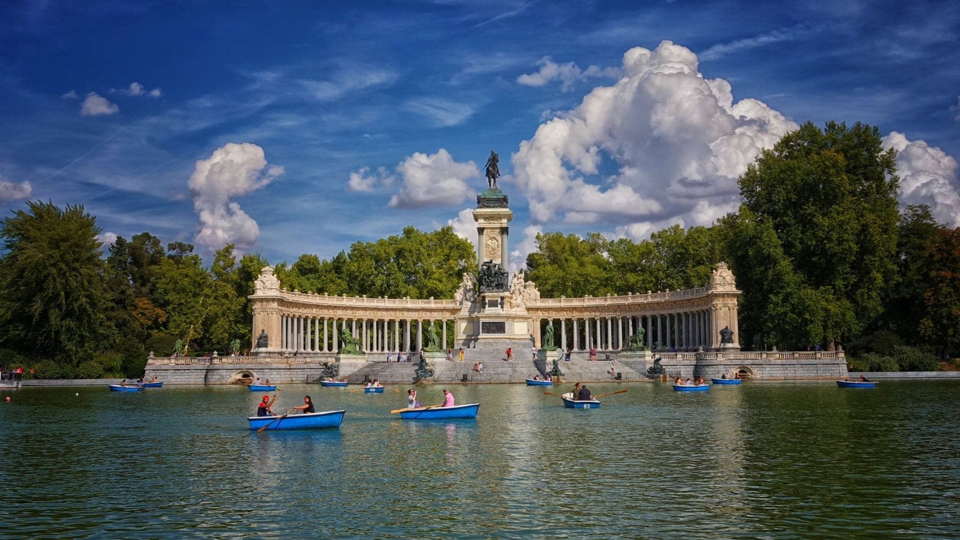 Łódki wiosłowe z rodzinami i dziećmi na dużym centralnym jeziorze przed pomnikiem Alfonso XII, Parque del Retiro, Madryt, w słoneczny dzień