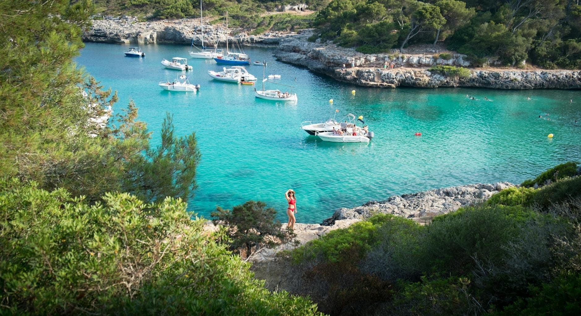 Abgelegene türkisfarbene Bucht auf Mallorca mit vor Anker liegenden Booten und Bäumen, die felsige Klippen einrahmen, als Highlight eines nur auf dem Wasserweg erreichbaren Reiseziels.