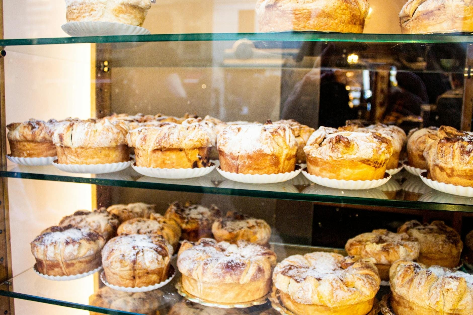 Vitrina de cristal llena de pasteles redondos espolvoreados con azúcar glas, que recuerdan las tradicionales ensaimadas mallorquinas en un ambiente de panadería.