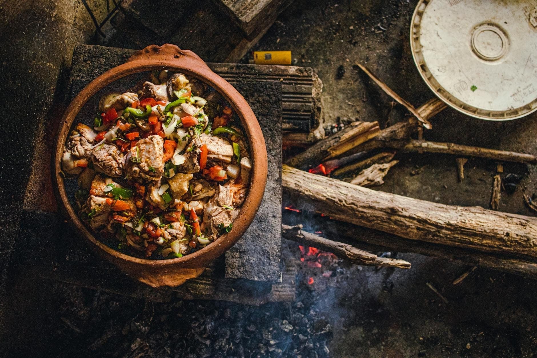 Una rústica olla de barro llena de carne y verduras cocinándose sobre un fuego de leña, evocando la tradicional cocina campesina mallorquina.