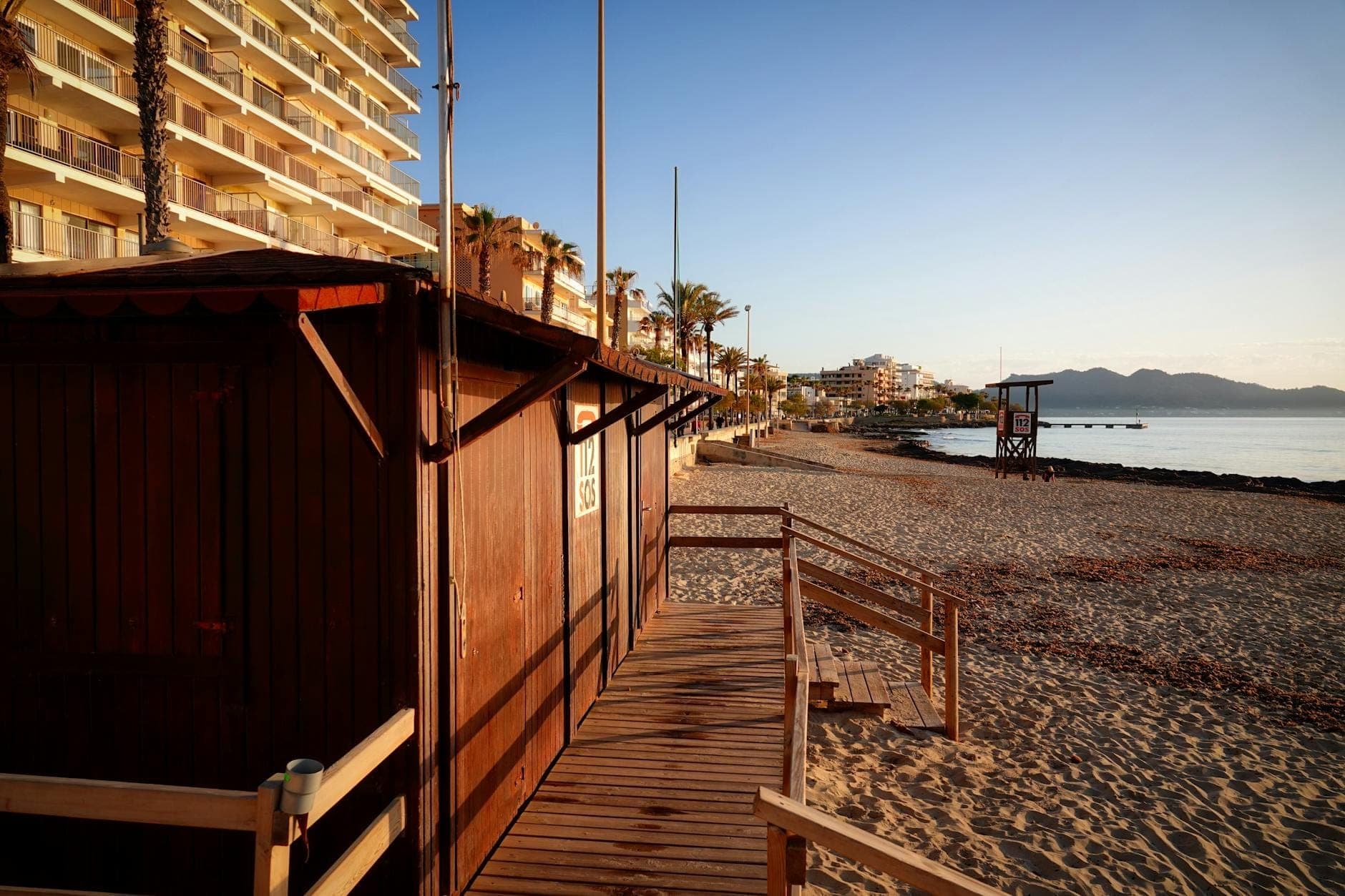 Vista nelle prime ore del mattino di una spiaggia quasi deserta a Mallorca con edifici di appartamenti e una cabina del bagnino, che suggerisce la tranquillità della bassa stagione.