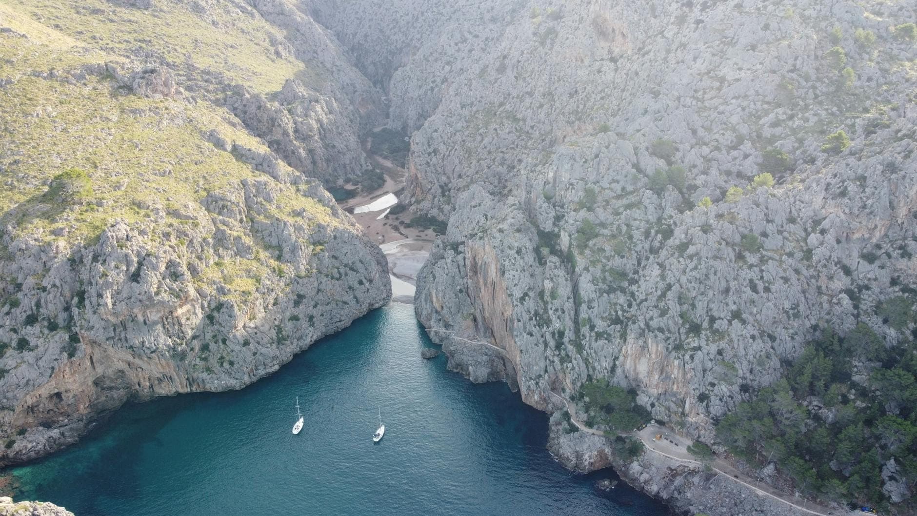 Eine dramatische Felsenschlucht mit türkisfarbenem Wasser, steilen Klippen und zwei kleinen verankerten Booten unten, die die wilde Naturlandschaft Mallorcas zeigt.