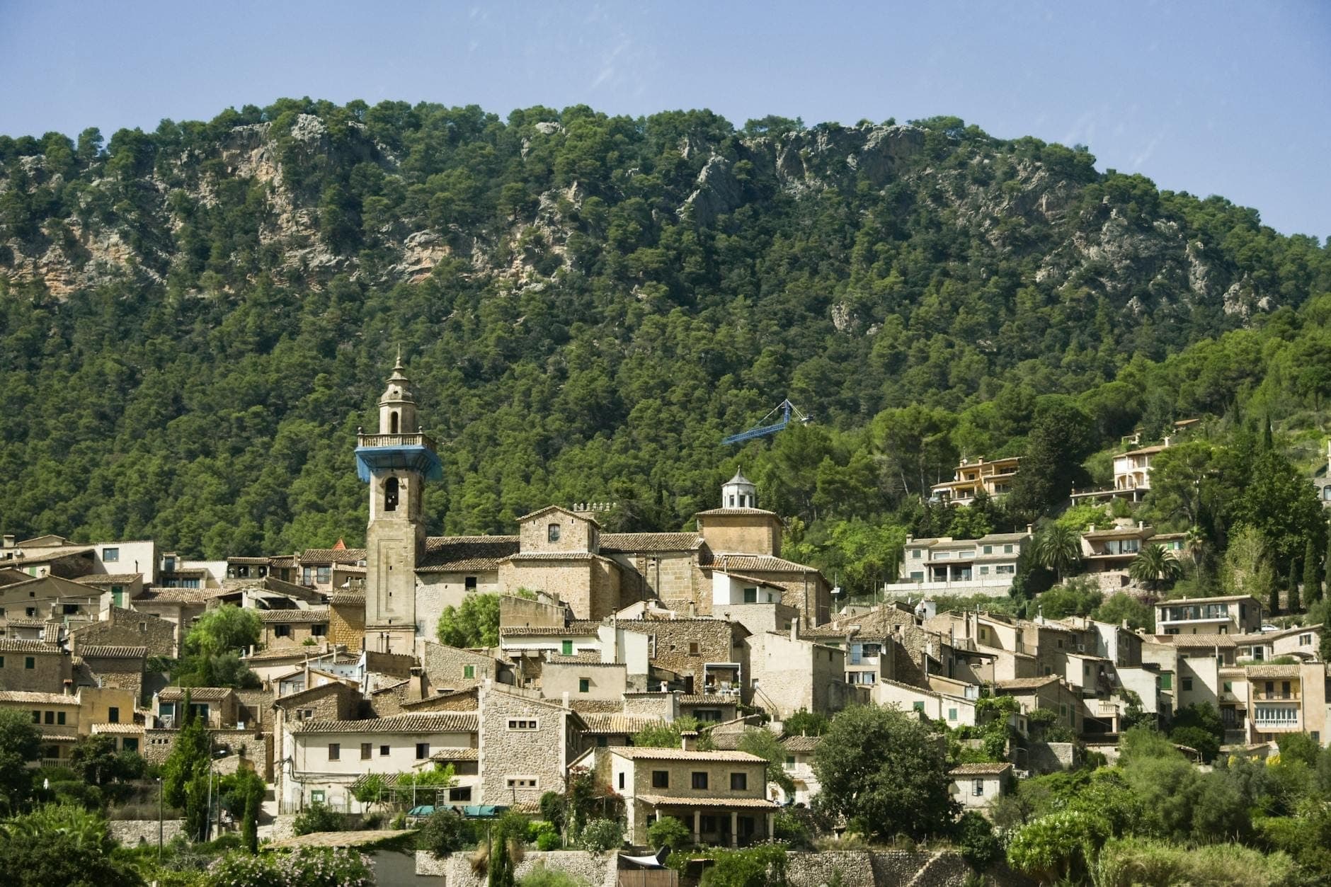 Il villaggio in pietra di Valldemossa adagiato ai piedi di una montagna verde nella regione della Tramuntana di Maiorca sotto un cielo azzurro.