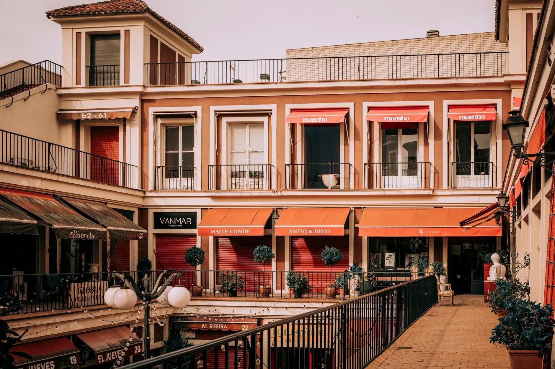 Attraente centro commerciale a due livelli a Mallorca con eleganti vetrine, tende da sole arancioni e piante in vaso, che suggerisce un'atmosfera da boutique.
