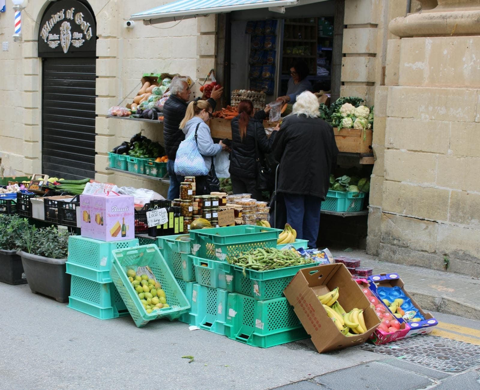 Piccolo gruppo di persone che acquistano prodotti freschi in un mercato di strada all'aperto in un villaggio mediterraneo in pietra.