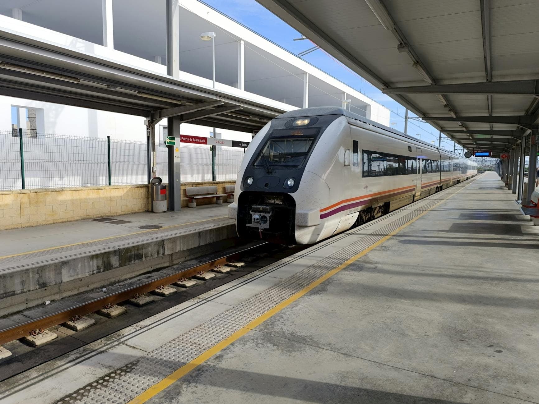 Trem regional moderno em uma plataforma aberta e ensolarada de uma estação ferroviária de Mallorca, pronto para embarque de passageiros.