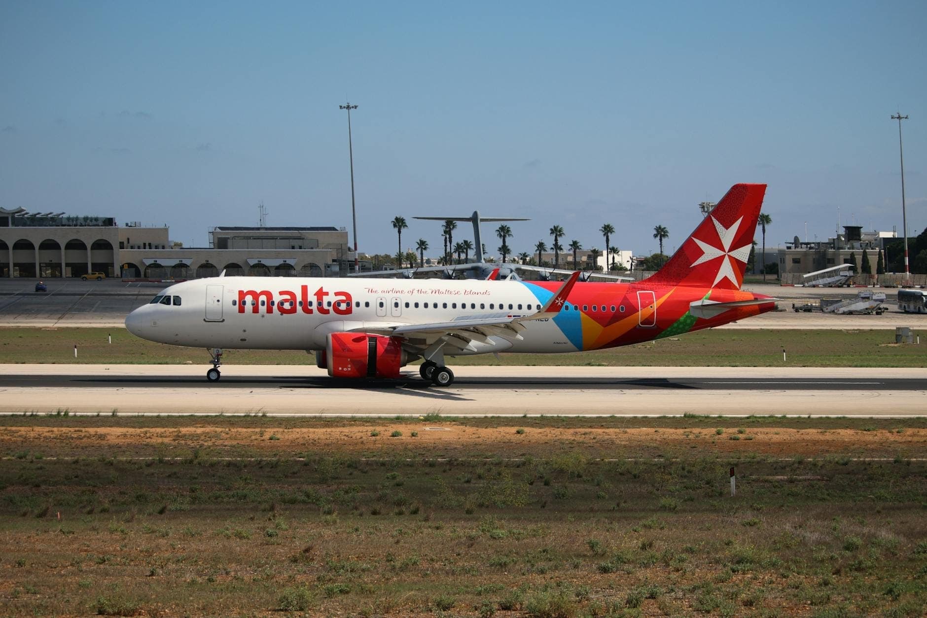 เครื่องบิน Air Malta บนรันเวย์ของ Malta International Airport โดยมีอาคารผู้โดยสารและต้นปาล์มอยู่เบื้องหลัง