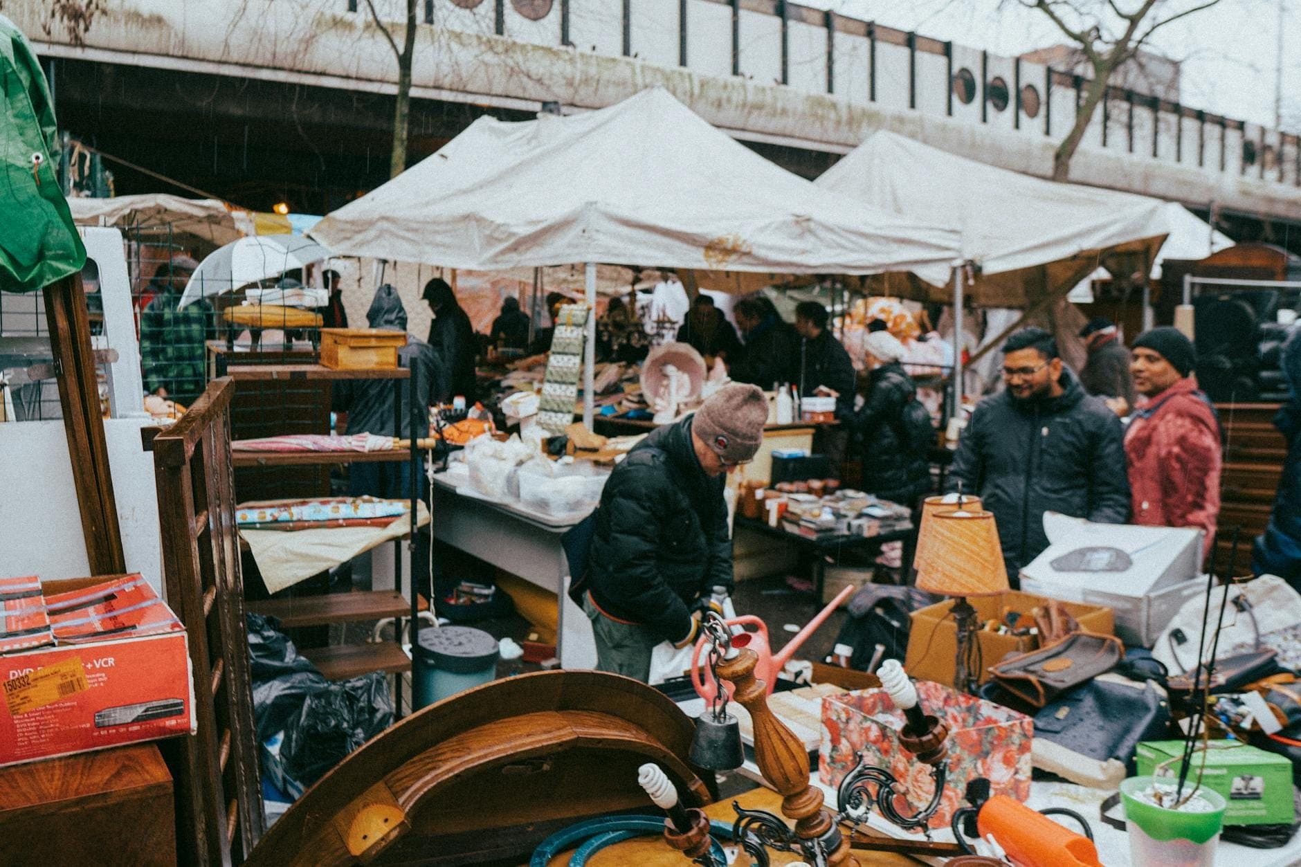Busy outdoor flea market with people browsing stalls under white tents, filled with vintage items, on a cloudy day in Paris.