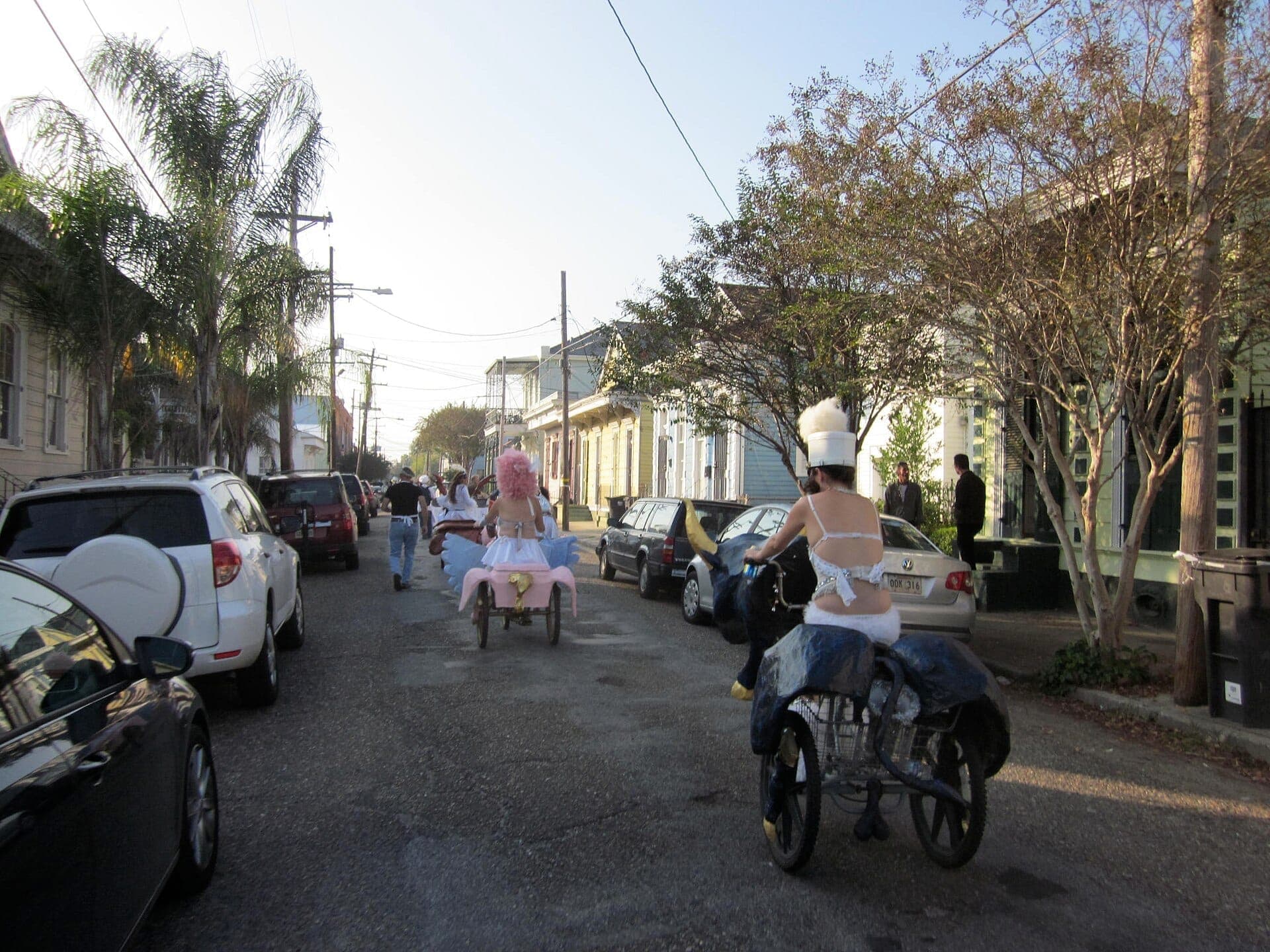Ciclistas fantasiados percorrem uma rua residencial ladeada de casas crioulas coloridas no bairro Marigny e Bywater de New Orleans.