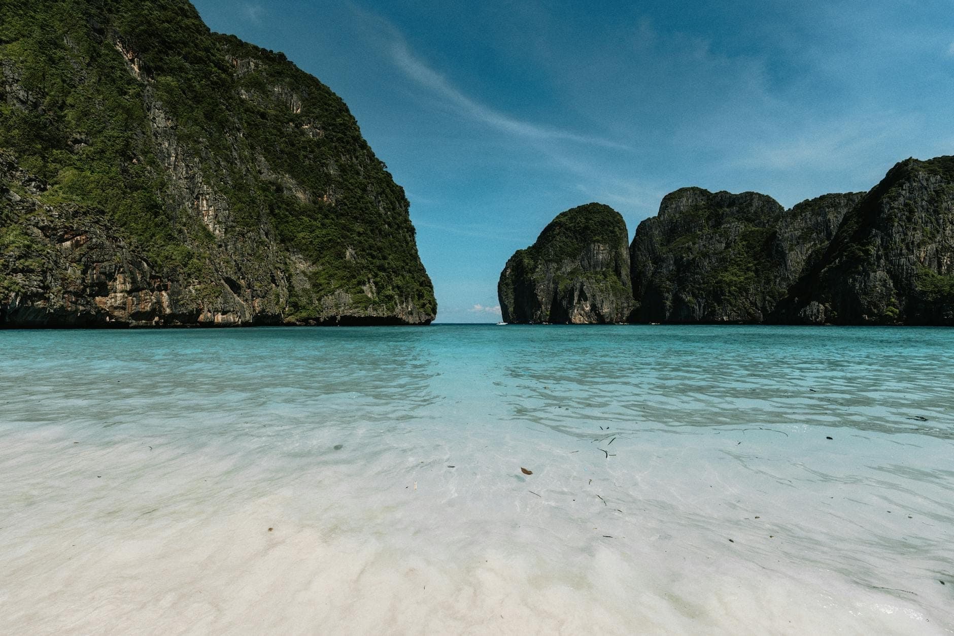 Vista panorámica de las aguas turquesas y la playa de arena blanca de Maya Bay, enmarcadas por imponentes acantilados de piedra caliza bajo un cielo azul despejado, sin personas visibles.
