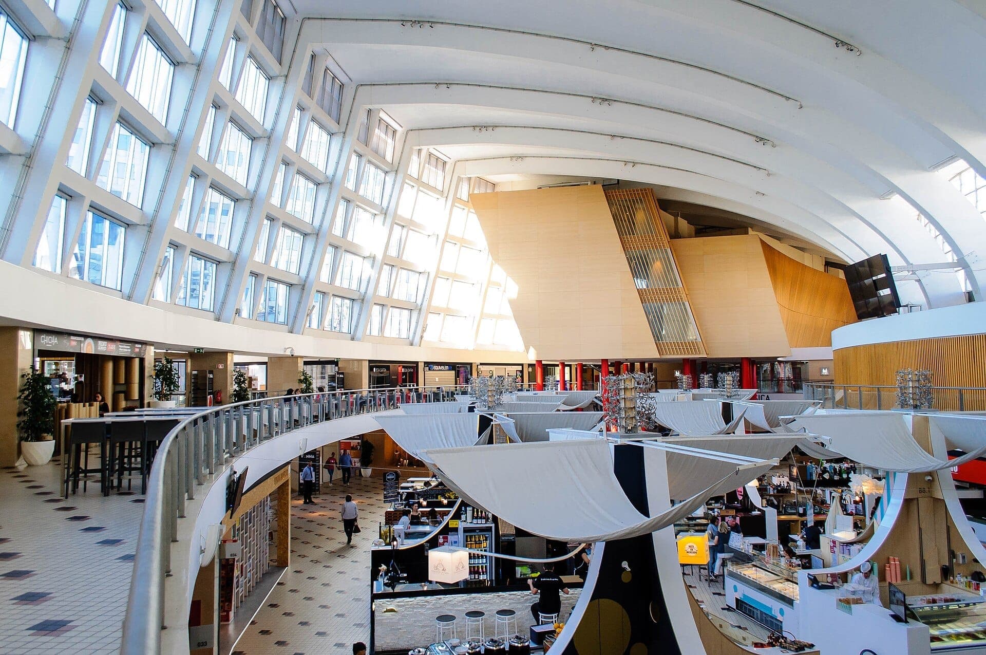 Vista interna del Mercado Bom Sucesso a Porto, con architettura moderna, grandi finestre curve e vari stand di cibo gourmet con visitatori.
