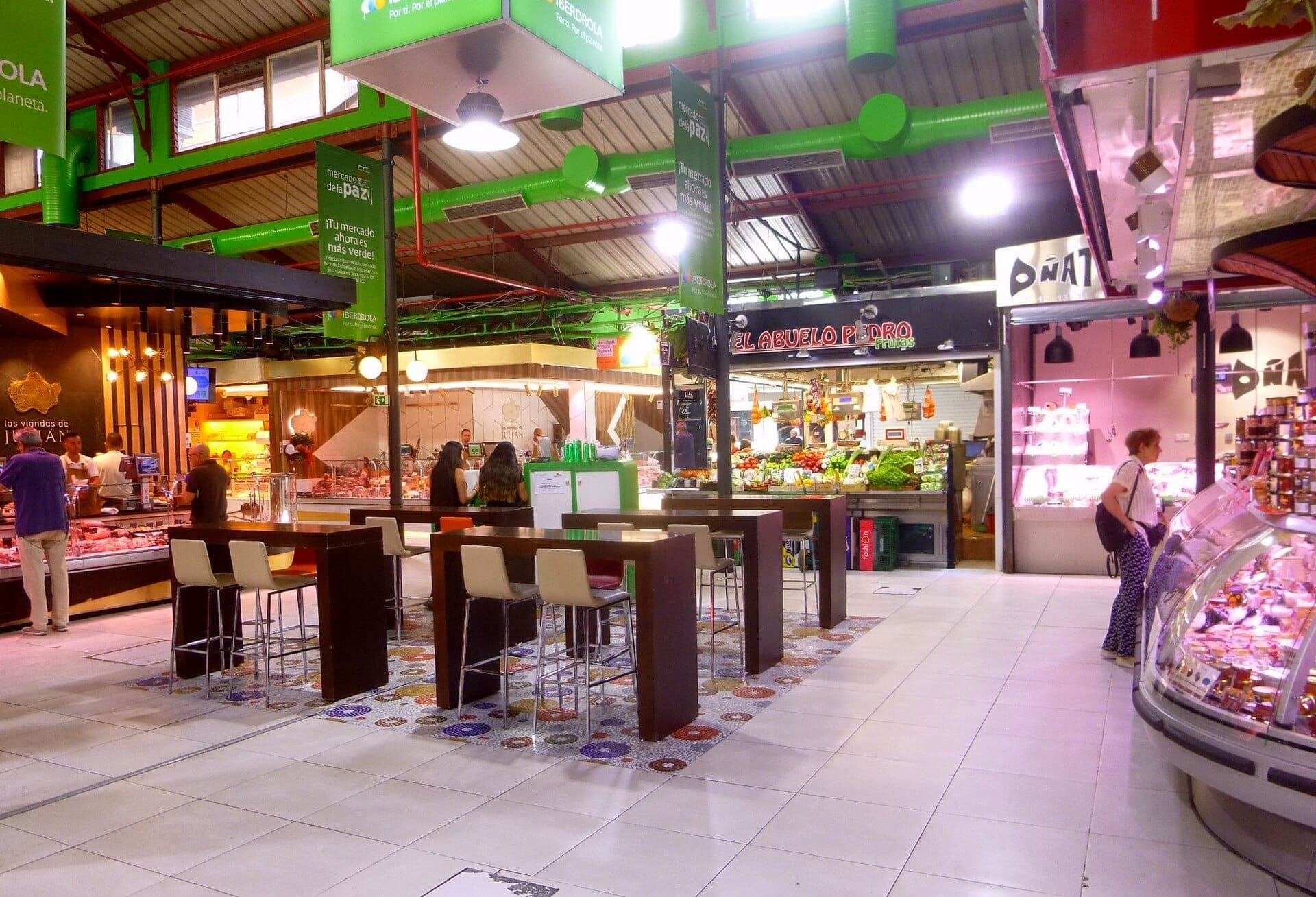 ภายในของ Mercado de La Paz ที่สว่างไสวพร้อมแผงอาหาร ผลิตผลสีสันสดใส และผู้คนที่กำลังช้อปปิ้งและรับประทานอาหารที่โต๊ะสมัยใหม่