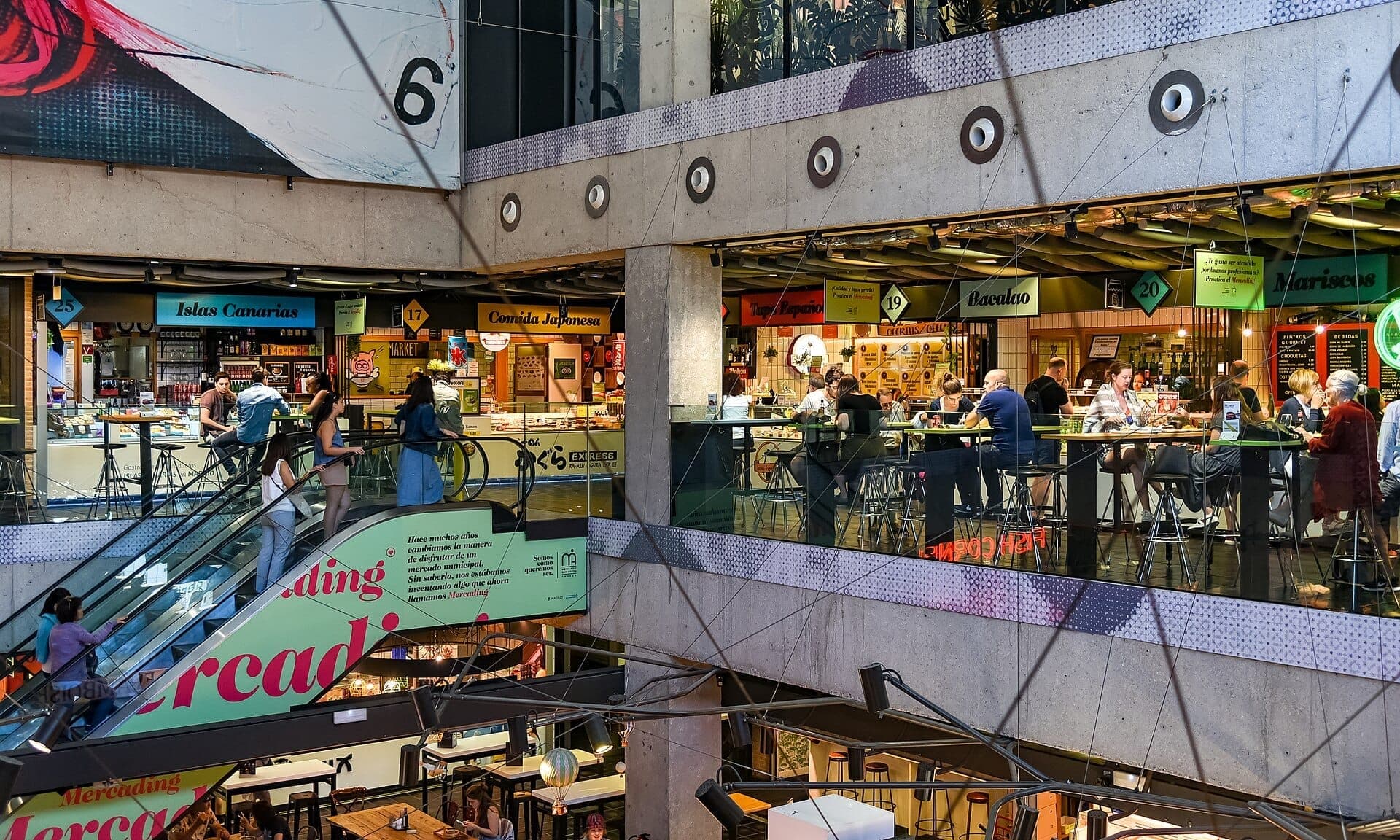 มุมมองภายในของ Mercado de San Antón แสดงให้เห็นแผงขายอาหารหลายแห่ง บันไดเลื่อน และผู้คนที่รับประทานอาหารบนโต๊ะสมัยใหม่ในหลายชั้น