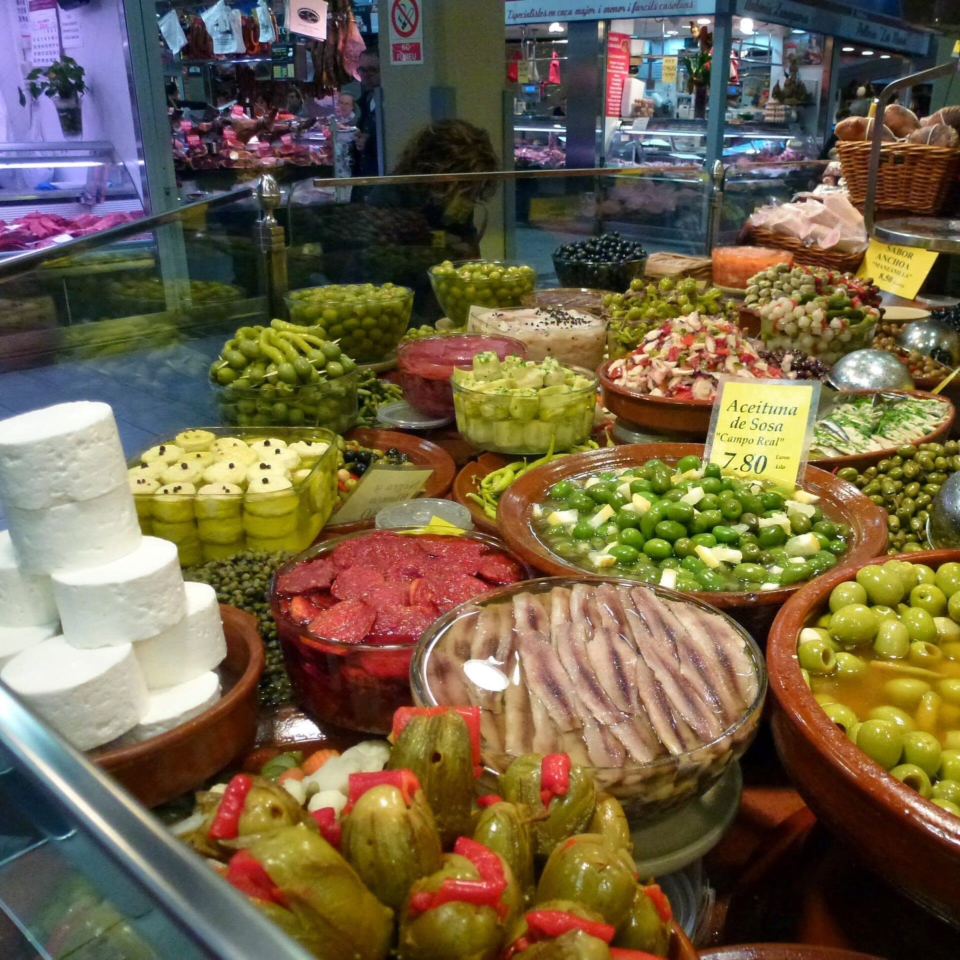 Buntes Sortiment aus Oliven, Käse und eingelegtem Gemüse an einem belebten Stand im Mercat de l'Olivar in Palma.