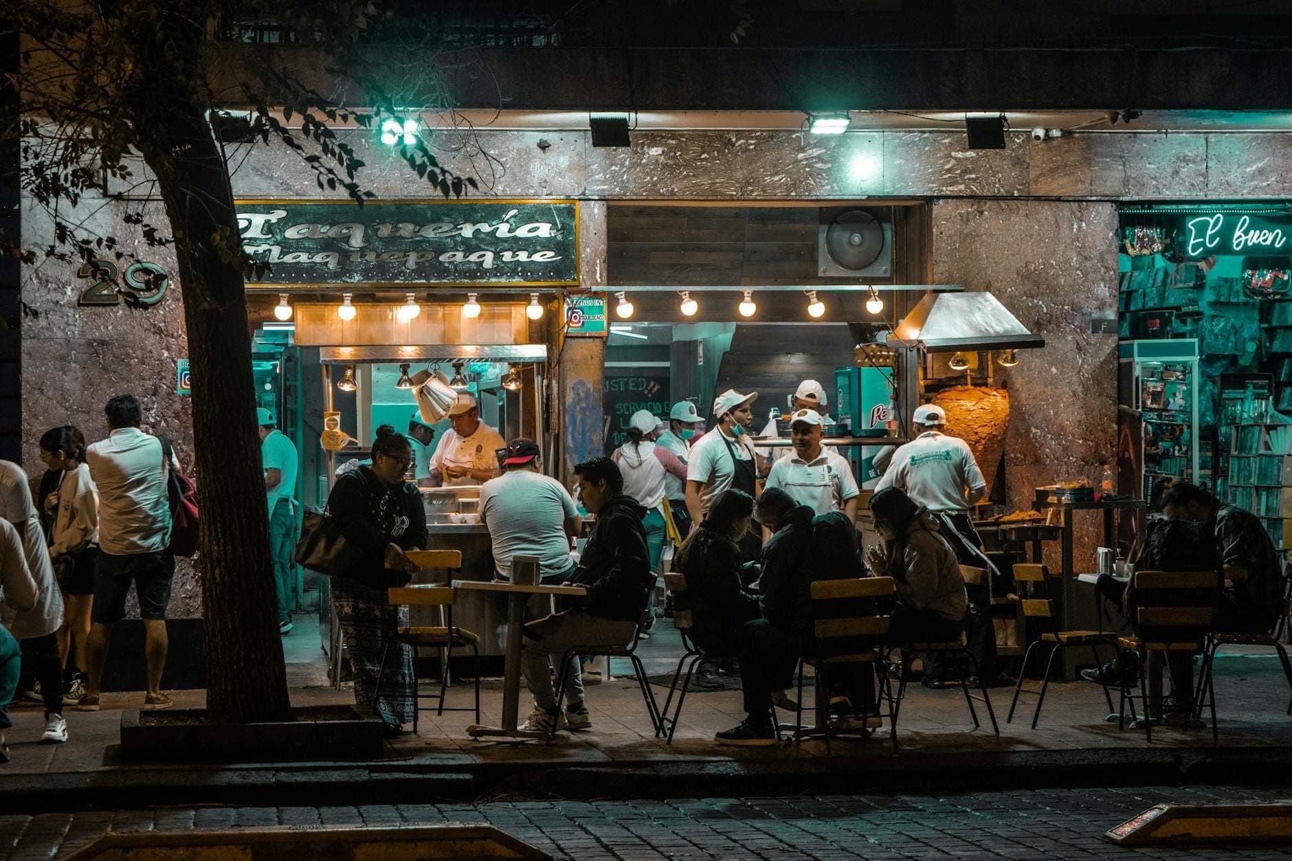 บรรยากาศยามค่ำคืนของร้านทาเกเรียที่คึกคักในเม็กซิโกซิตี้ มีผู้คนรับประทานอาหารด้านนอกและพ่อครัวทำงานอยู่ภายในท่ามกลางแสงไฟสว่างไสว