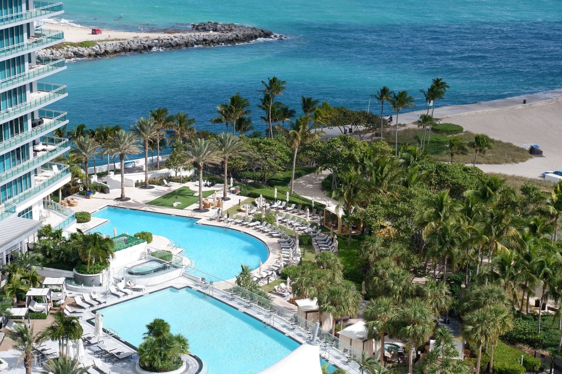 Aerial view of a luxury Miami oceanfront resort with multiple pools, palm trees, cabanas, and direct beach access to turquoise water and white sand.