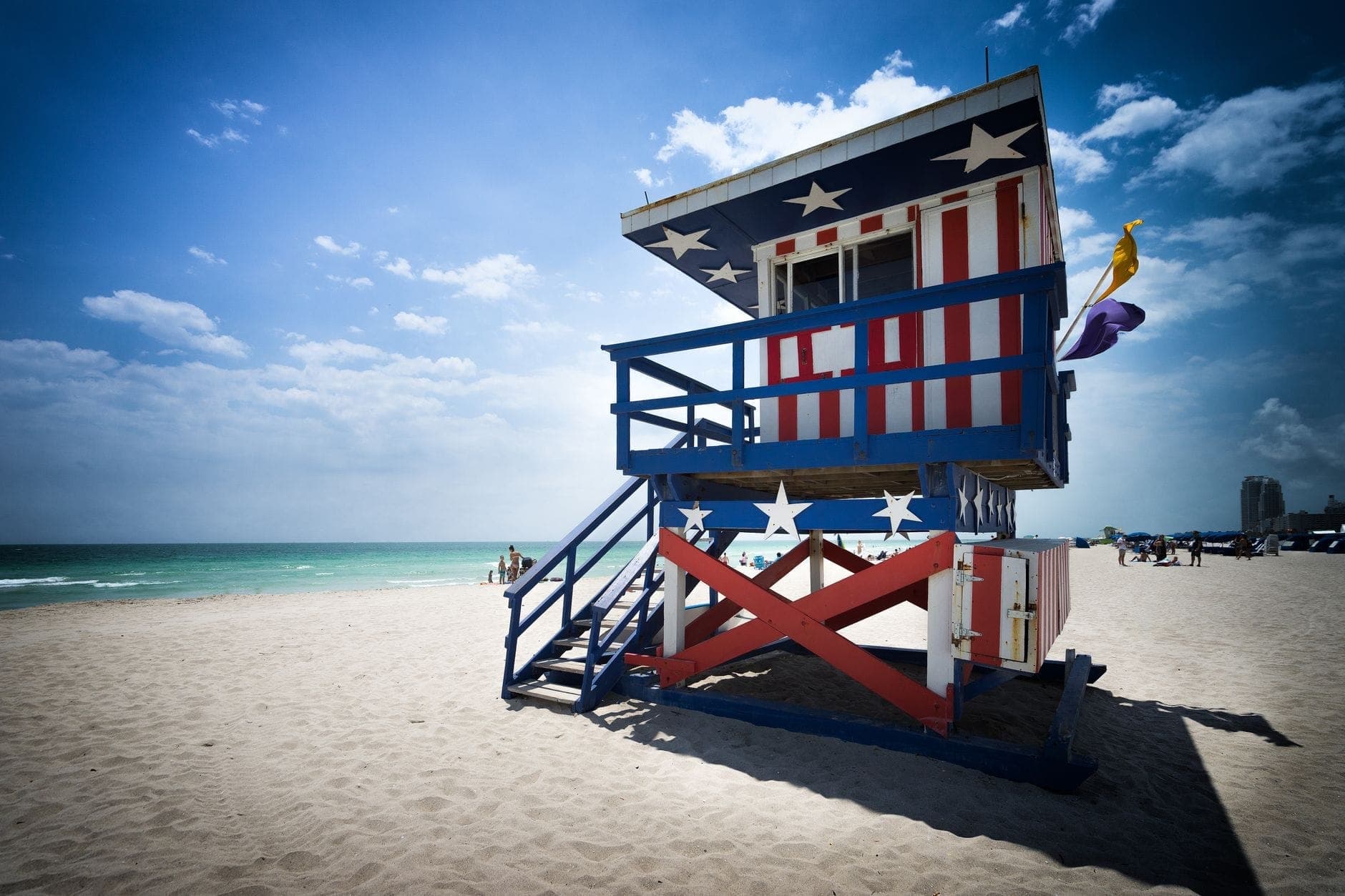 Patriotic red, white, and blue striped lifeguard tower on Miami Beach with clear skies, sand, and ocean, evoking safety and iconic local vibe.