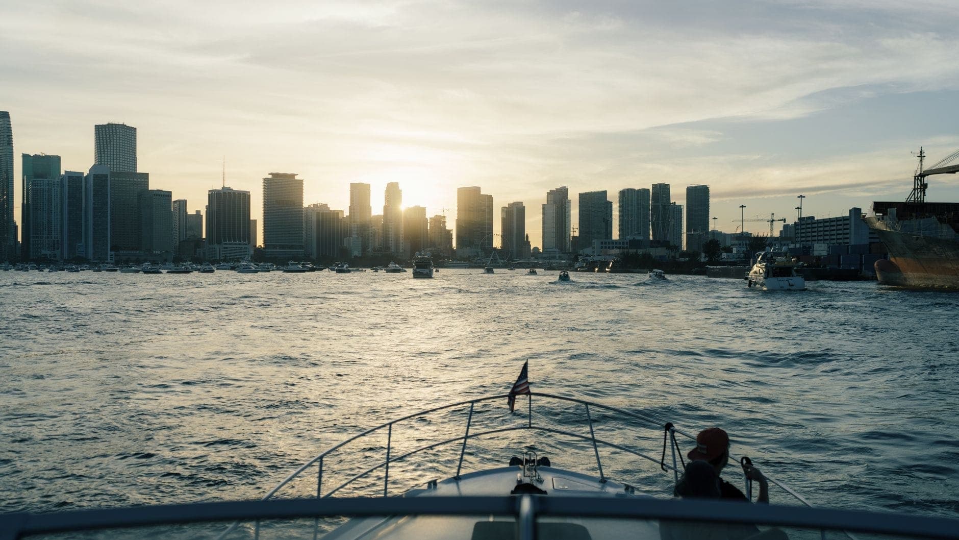 View from the bow of a boat heading toward Miami skyline at sunset with surrounding boats on the water.