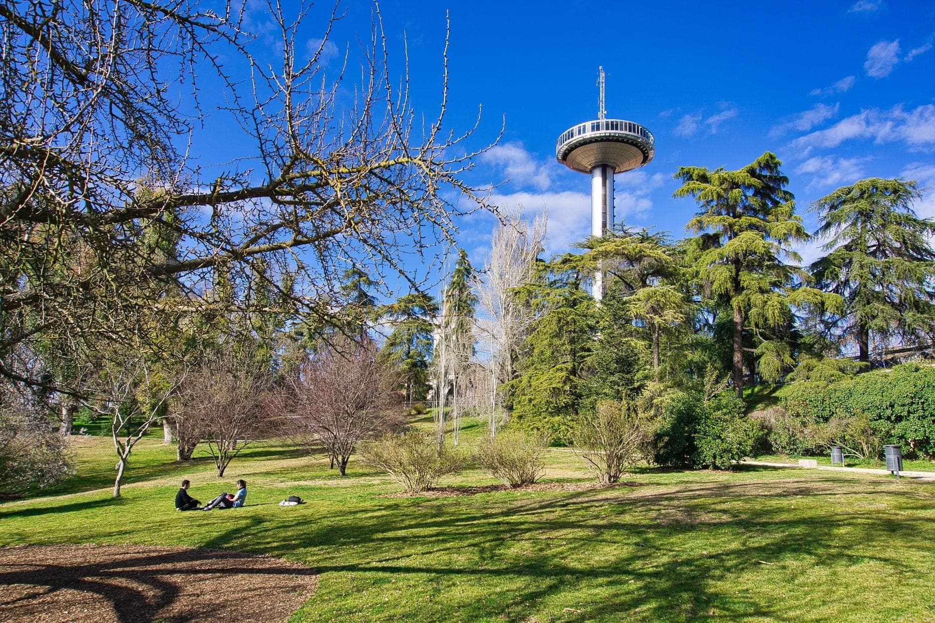 หอคอย Faro de Moncloa สูงเด่นกลางสวนสีเขียวในมาดริด คนพักผ่อนบนสนามหญ้า ท้องฟ้าสีฟ้าสดใส