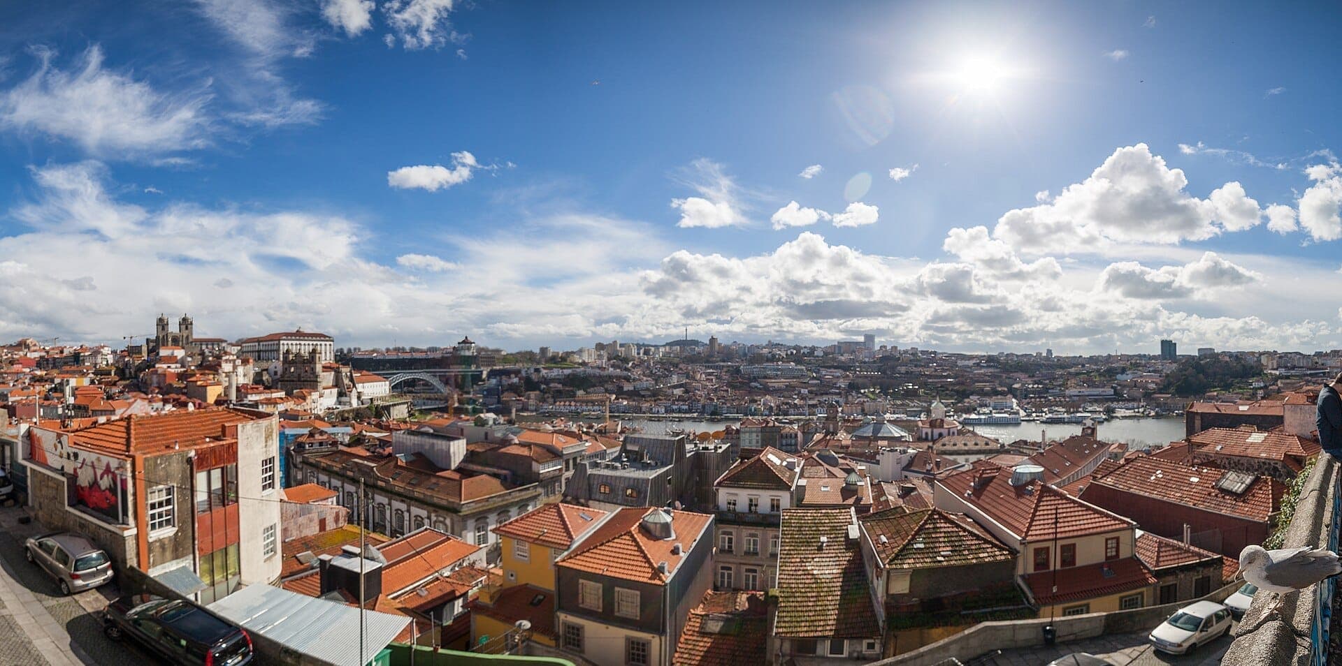 Ampia vista dal Miradouro da Vitória sugli edifici dai tetti rossi di Porto, il fiume Douro e il Ponte Dom Luís I sotto un cielo azzurro brillante.