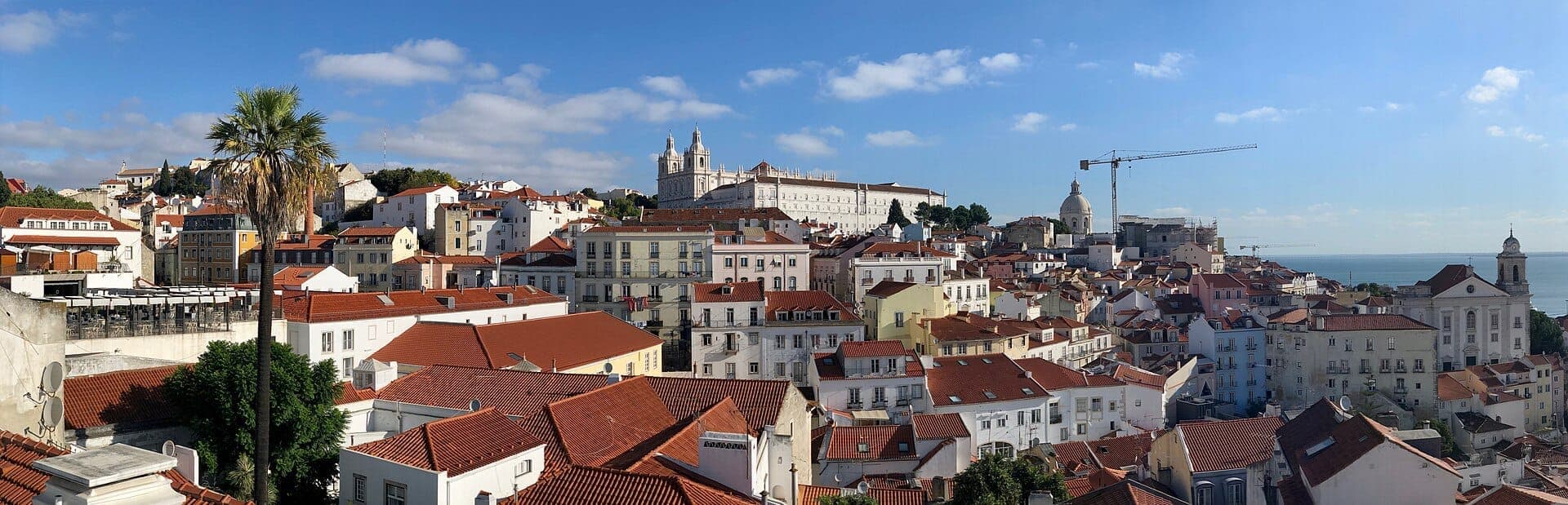 Vista panorâmica do Miradouro das Portas do Sol, destacando os telhados vermelhos de Alfama, a cúpula branca de São Vicente de Fora e o rio Tejo.