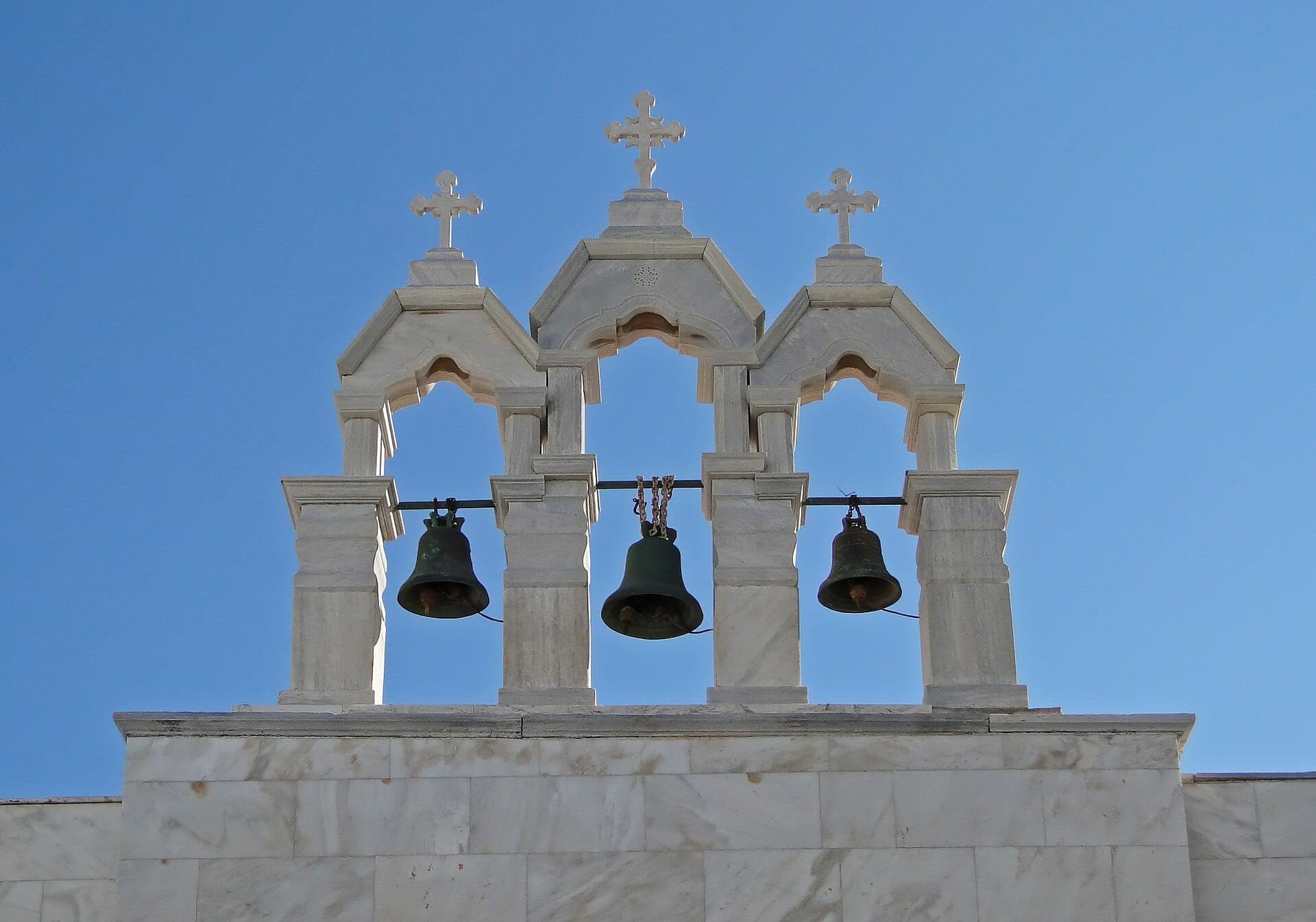 Weißer Marmorglockenturm mit drei Glocken und Kreuzen im Kloster Panagia Tourliani vor dem klaren blauen Himmel von Mykonos.